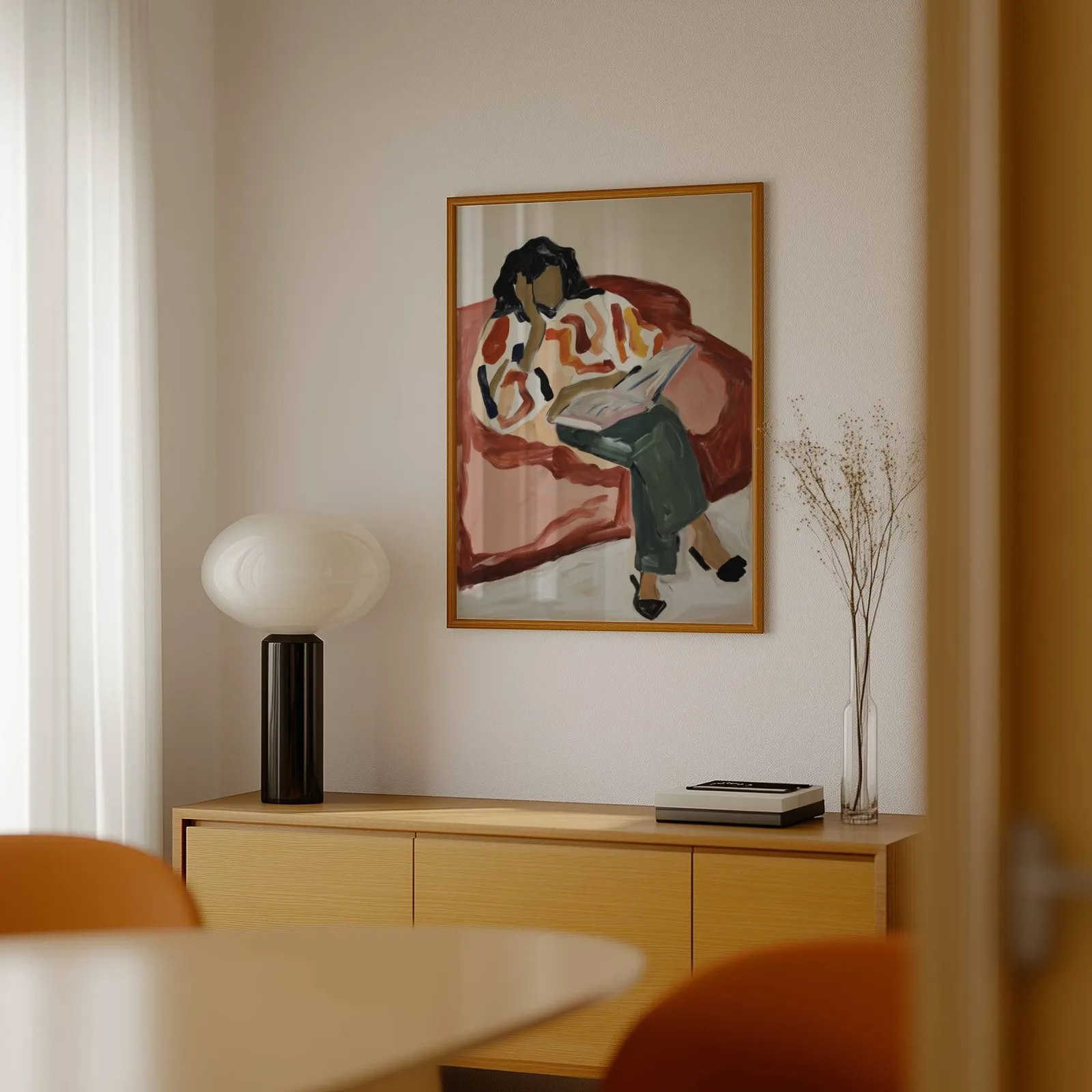 terracotta woman reading wall art, above a light wood sideboard beside a bulbous black lamp
