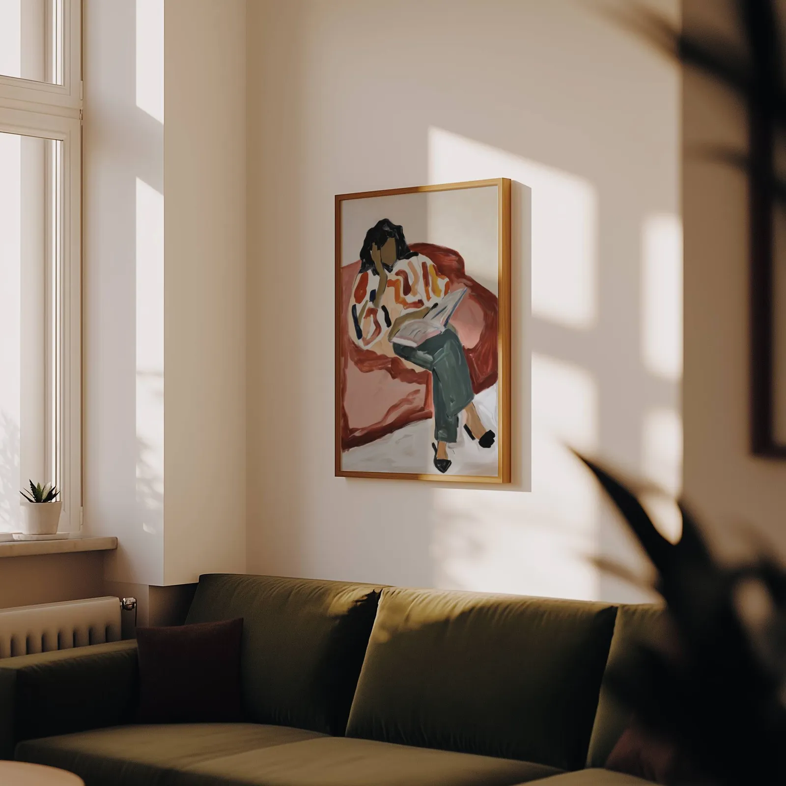 terracotta woman reading wall art, above an olive velvet sofa in raking afternoon light