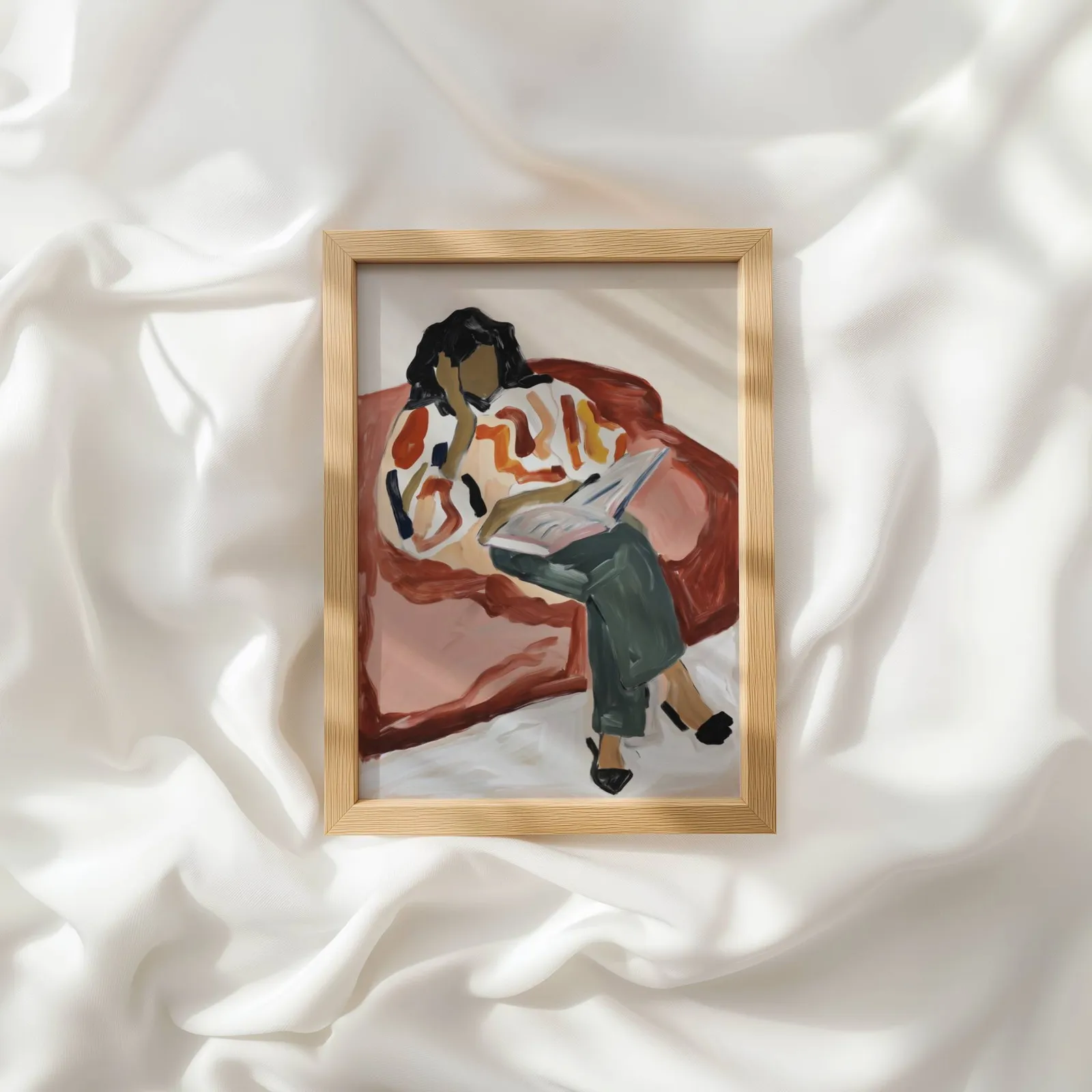 terracotta woman reading wall art, resting atop rumpled white silky fabric