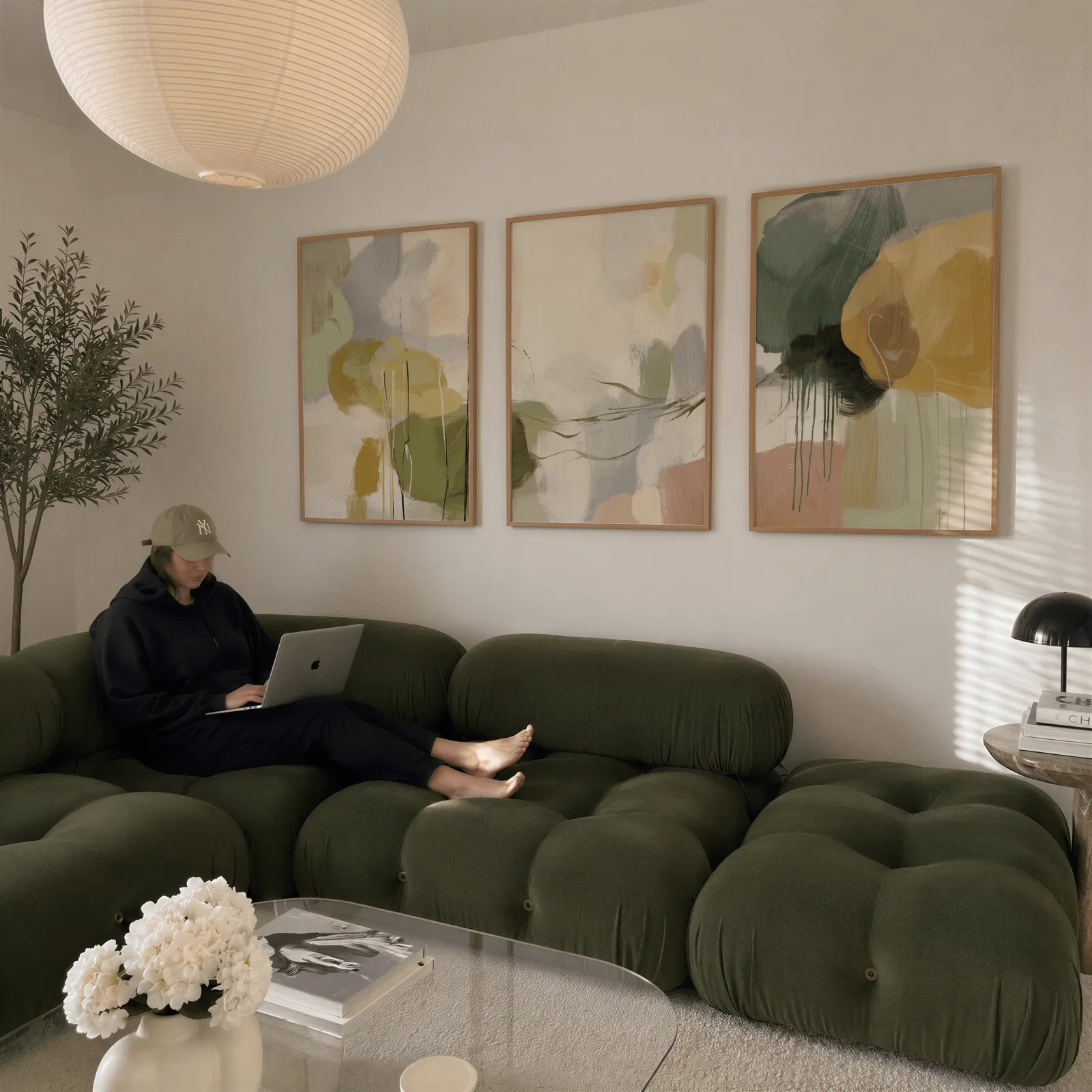 green and gold abstract triptych wall art, above a plush olive velvet sectional beneath a paper lantern light