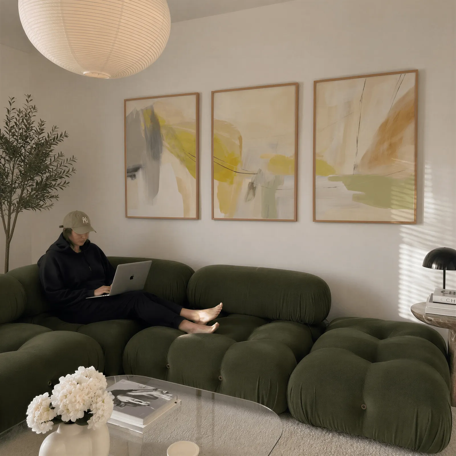 yellow and beige abstract wall art set of 3, above a plush olive velvet sectional beneath a paper lantern light