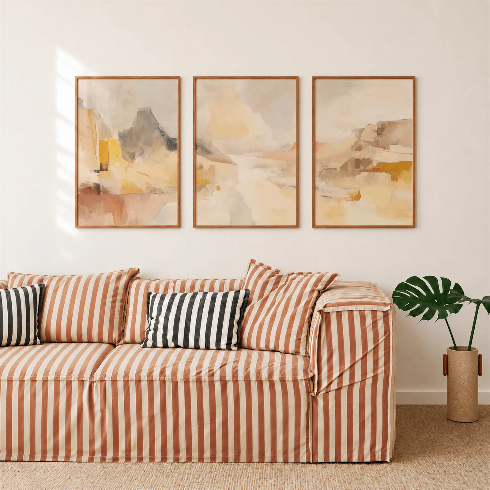 amber abstract landscape triptych wall art, above a rust-striped sofa beside a potted monstera