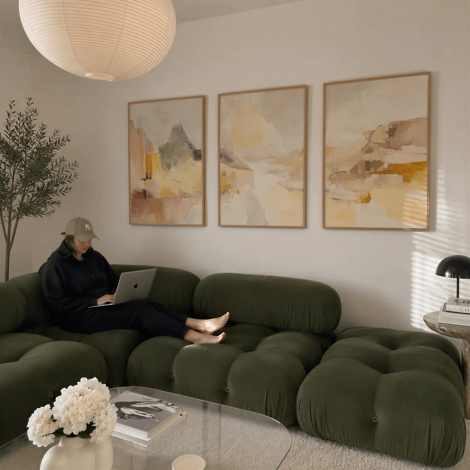 amber abstract landscape triptych wall art, above a plush olive velvet sectional beneath a paper lantern light