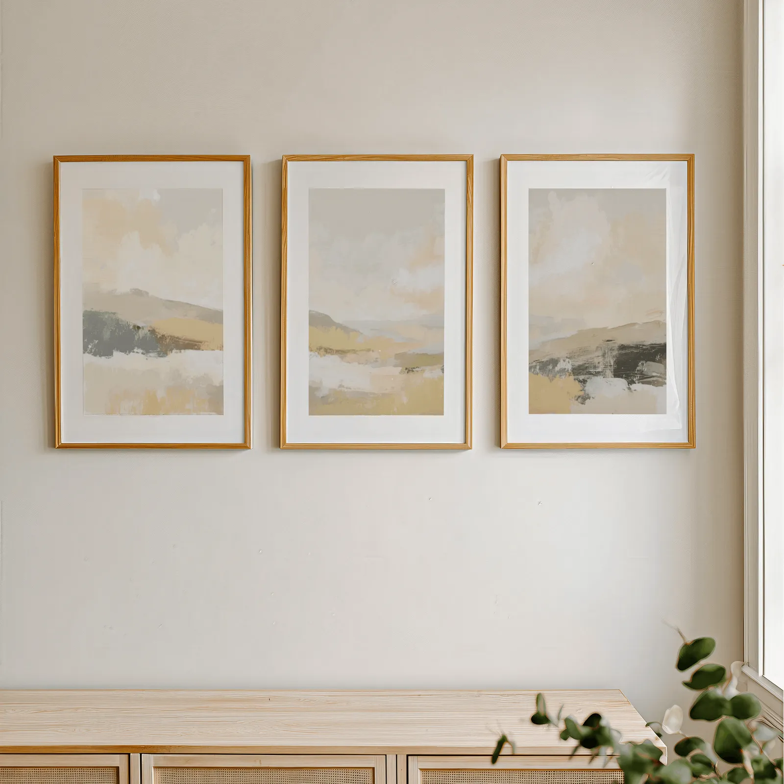 beige abstract landscape triptych wall art, in a row above a light wooden sideboard near a window