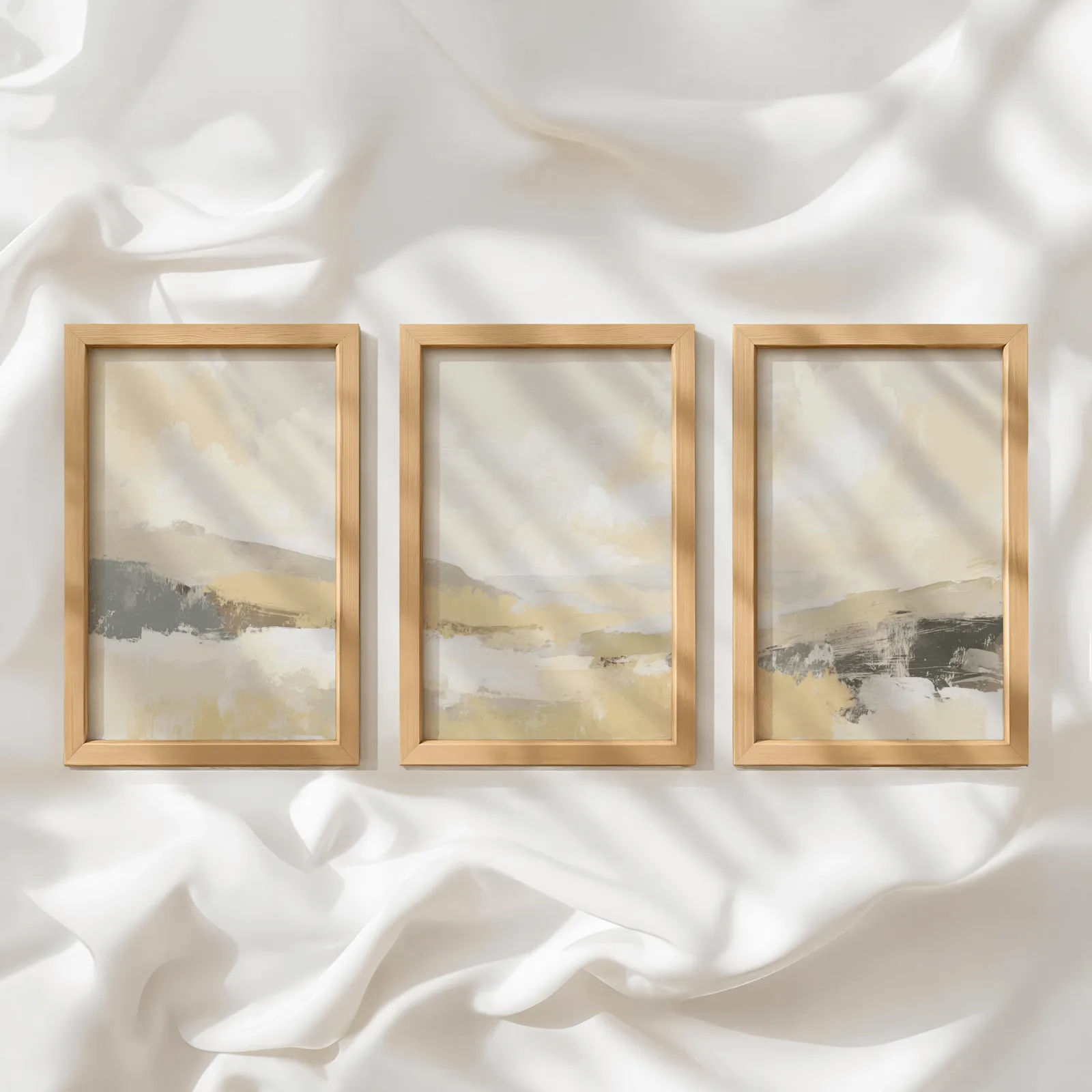 beige abstract landscape triptych wall art, in a row atop rumpled white silky fabric