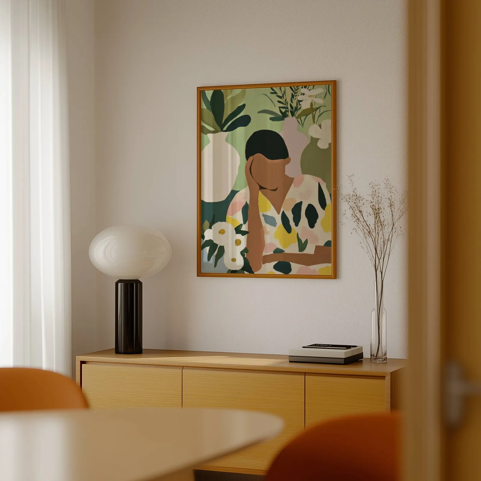 botanical woman wall art in green and cream, above a light wood sideboard beside a bulbous black lamp