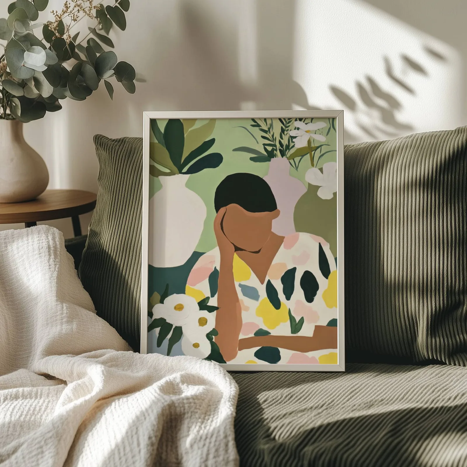 botanical woman wall art in green and cream, propped on an olive corduroy sofa beside a eucalyptus vase
