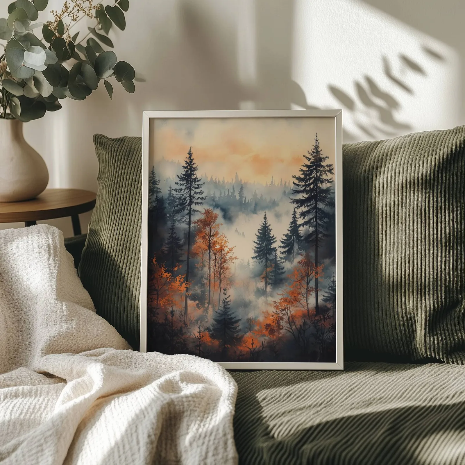 moody misty forest wall art in orange and grey, propped on an olive corduroy sofa beside a eucalyptus vase