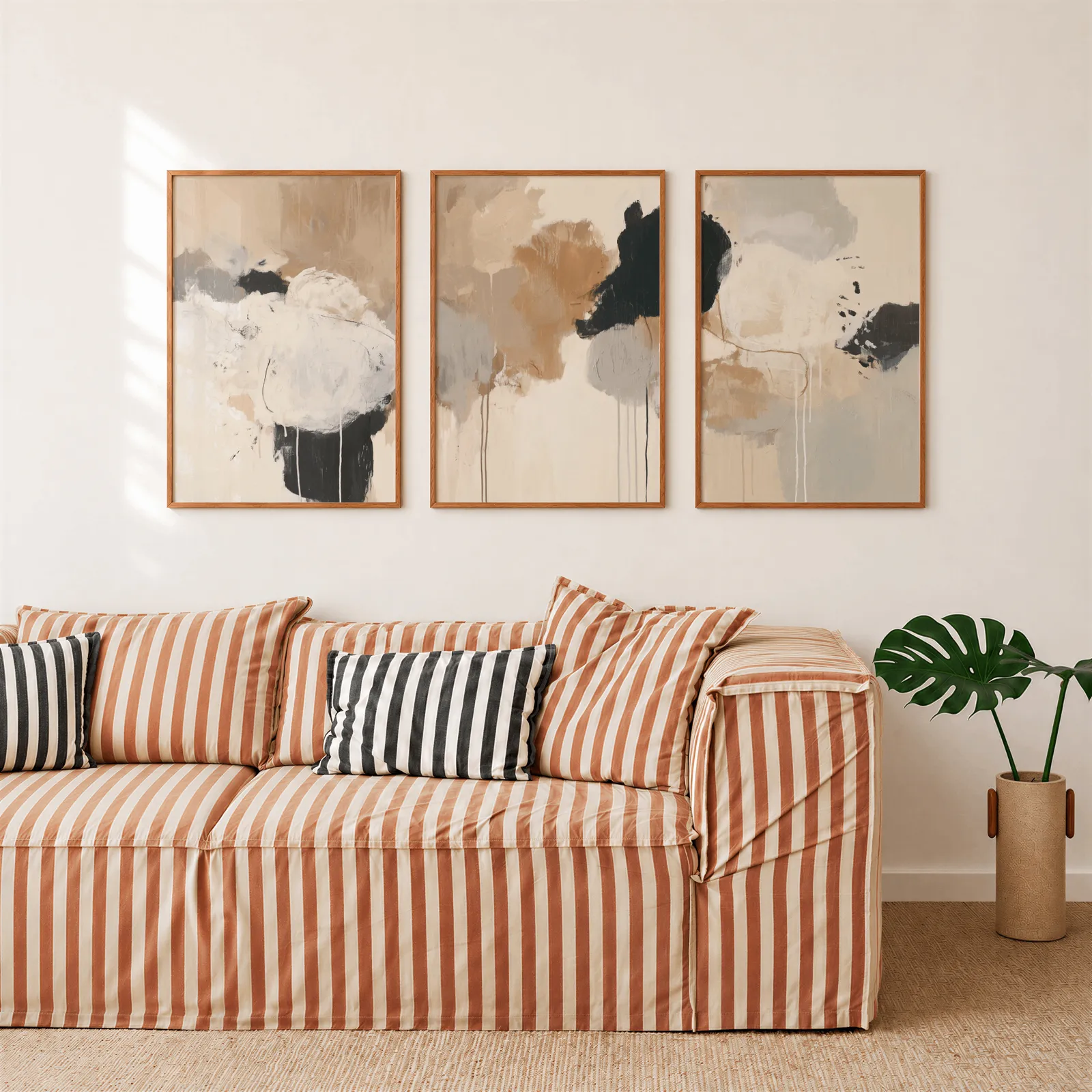 neutral abstract triptych wall art in beige and black, above a rust-striped sofa beside a potted monstera