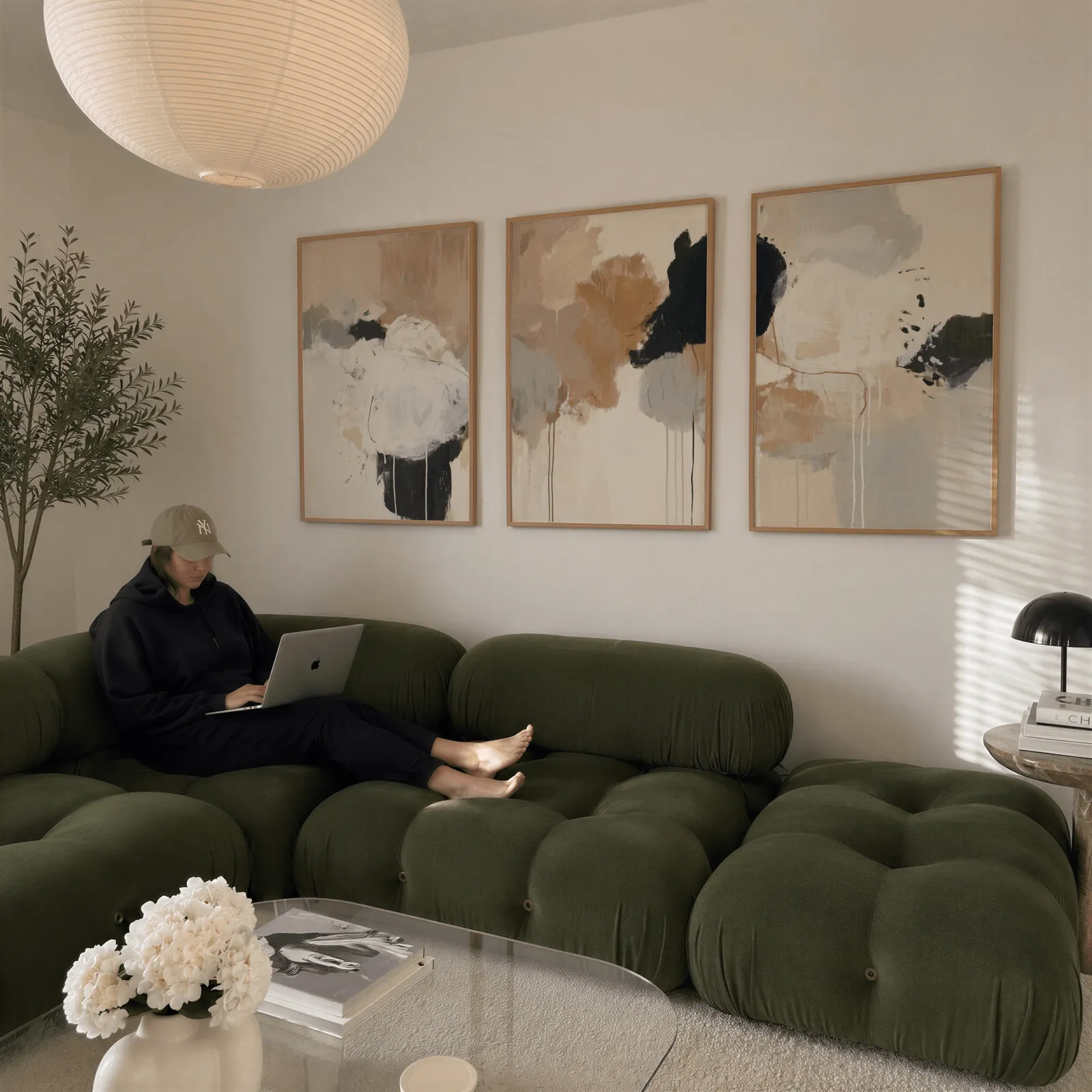 neutral abstract triptych wall art in beige and black, above a plush olive velvet sectional beneath a paper lantern light