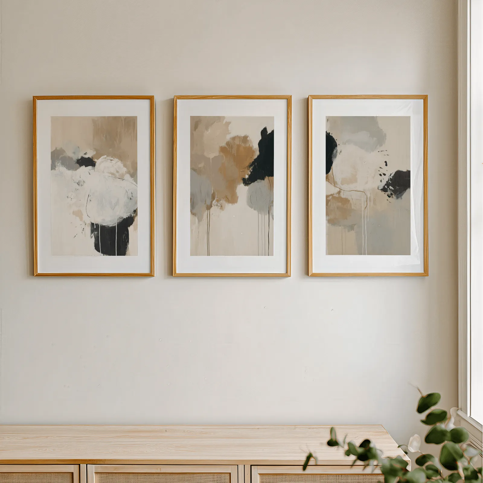 neutral abstract triptych wall art in beige and black, in a row above a light wooden sideboard near a window