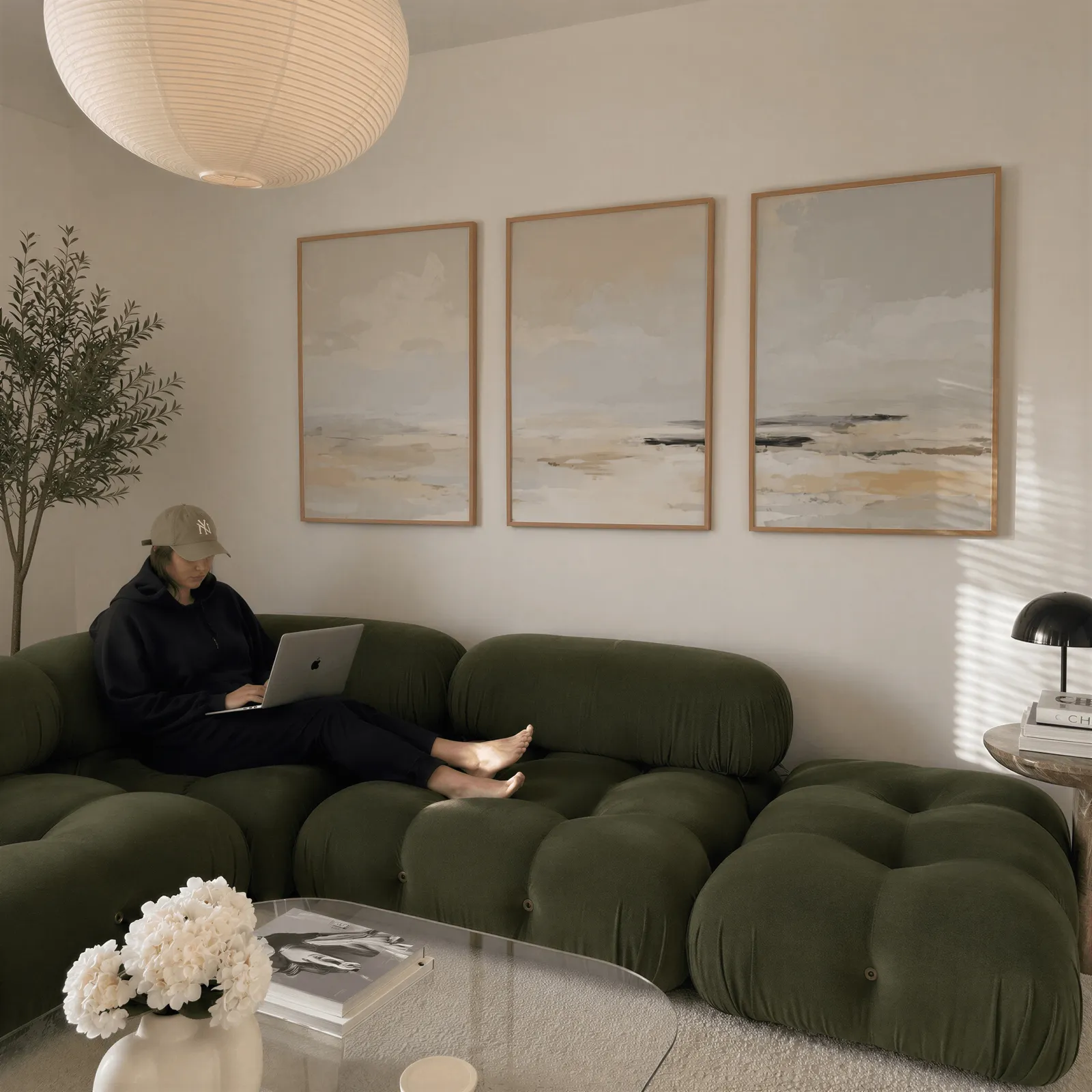 neutral coastal landscape triptych wall art, above a plush olive velvet sectional beneath a paper lantern light
