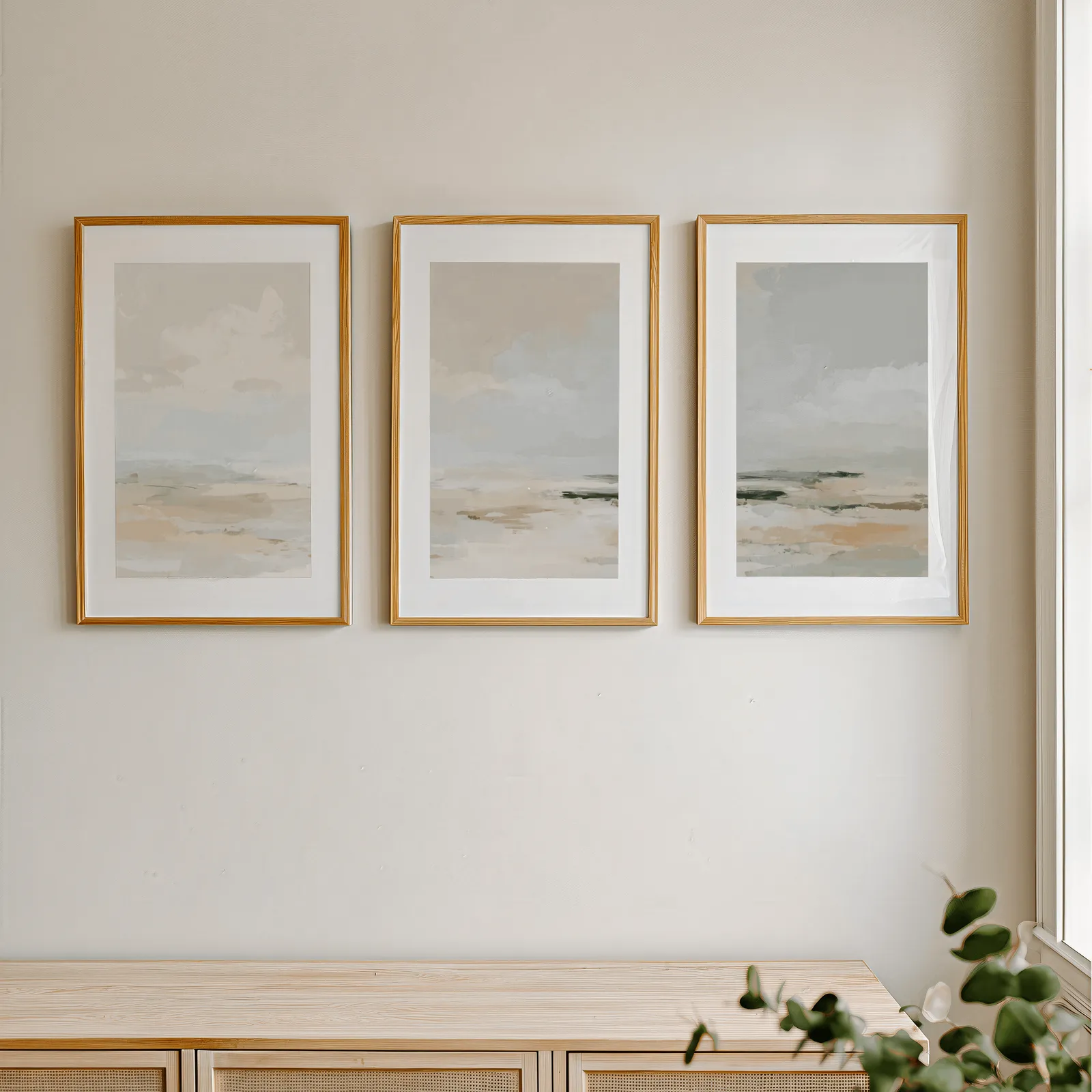 neutral coastal landscape triptych wall art, in a row above a light wooden sideboard near a window