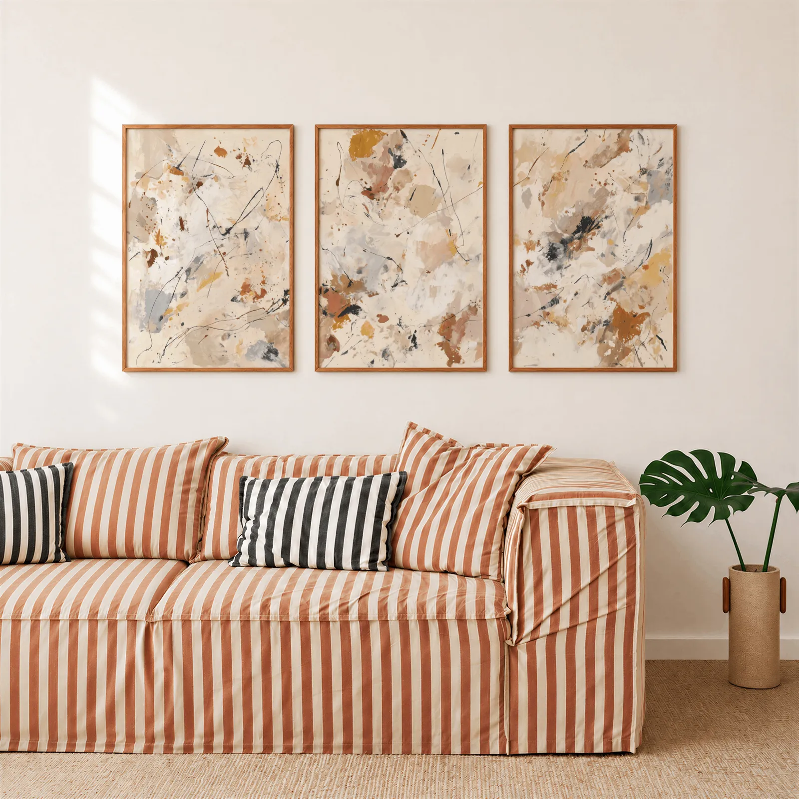 abstract neutral wall art set of 3 in terracotta and grey, above a rust-striped sofa beside a potted monstera