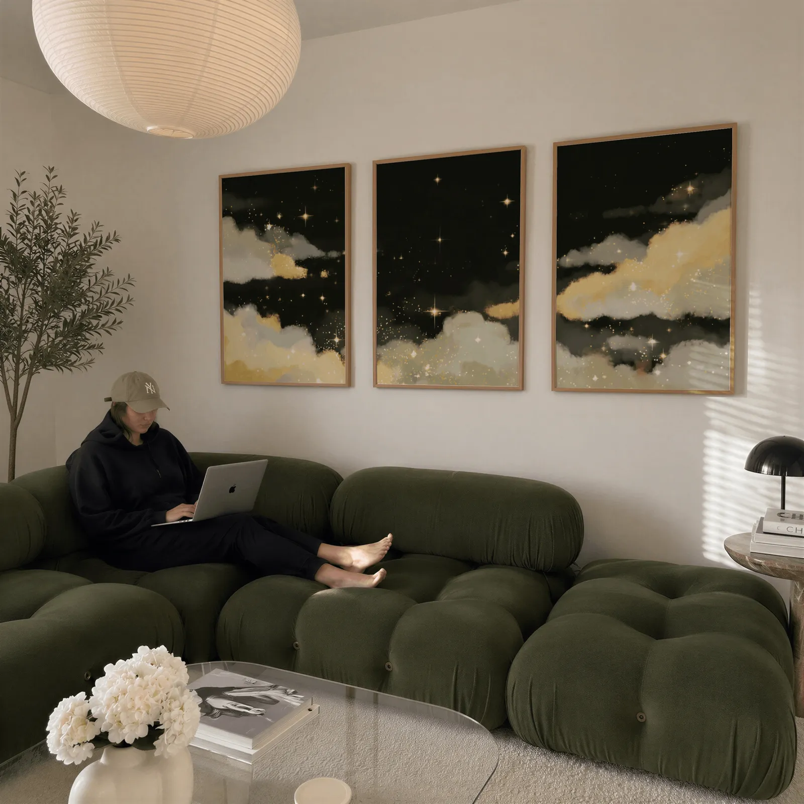 black and gold starry sky triptych wall art, above a plush olive velvet sectional beneath a paper lantern light
