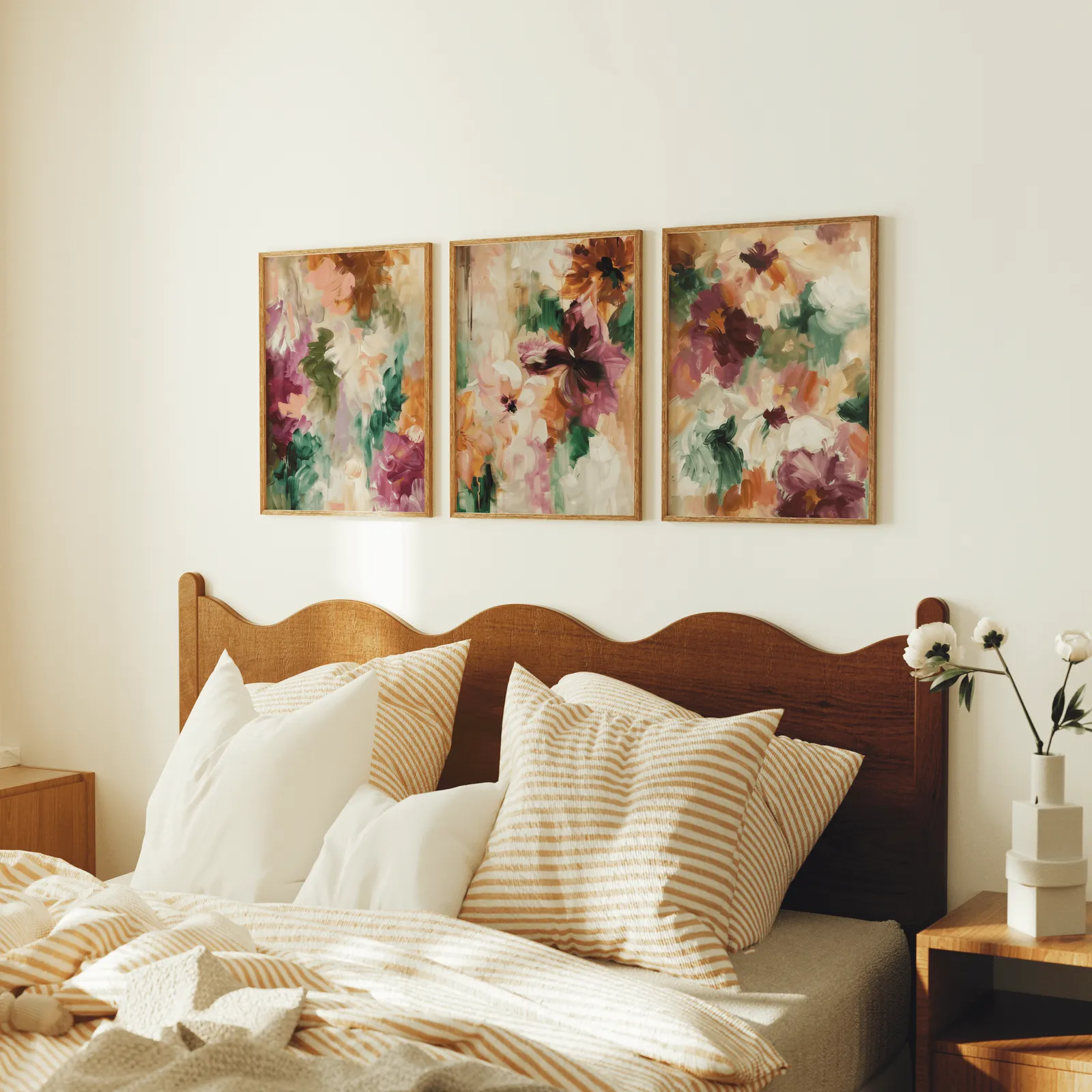 colorful floral triptych wall art in burgundy and green, above a scalloped wooden headboard with striped pillows
