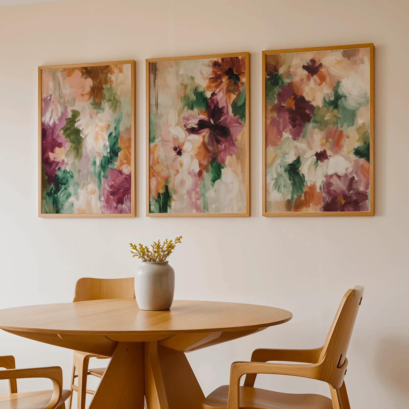 colorful floral triptych wall art in burgundy and green, above a round wooden table with a stoneware vase