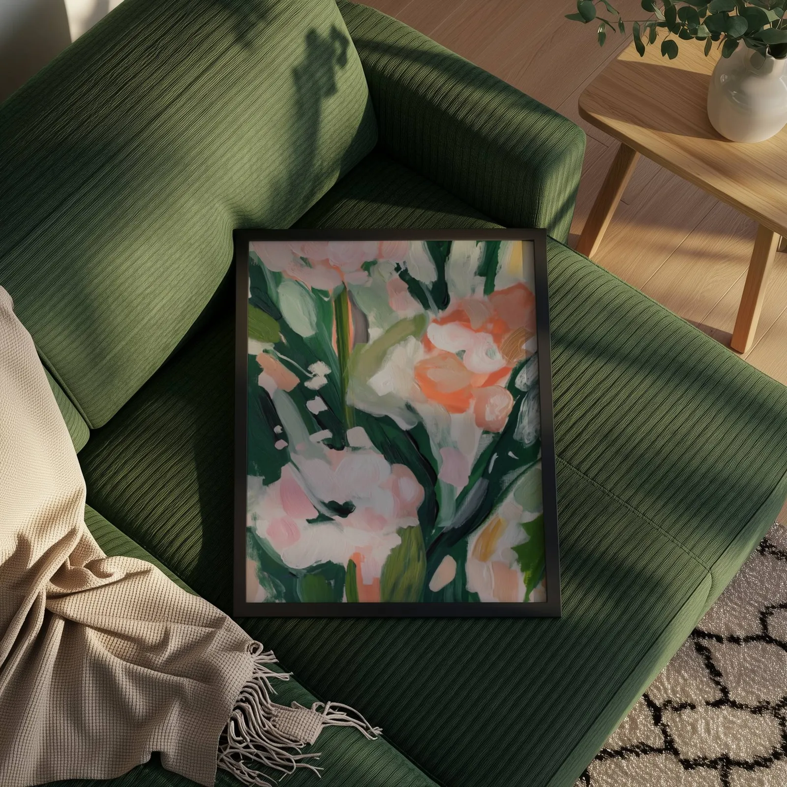 pink floral botanical wall art, propped on a ribbed olive-green sofa beside a fringed throw