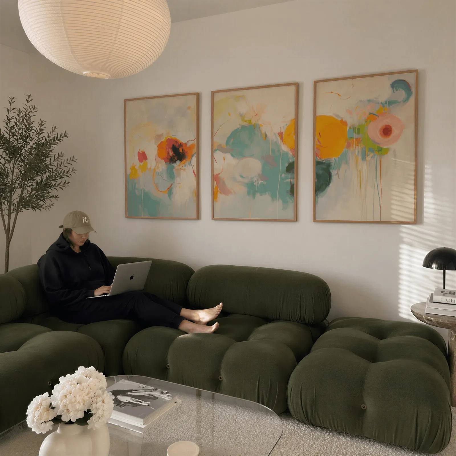 colorful abstract triptych wall art, above a plush olive velvet sectional beneath a paper lantern light