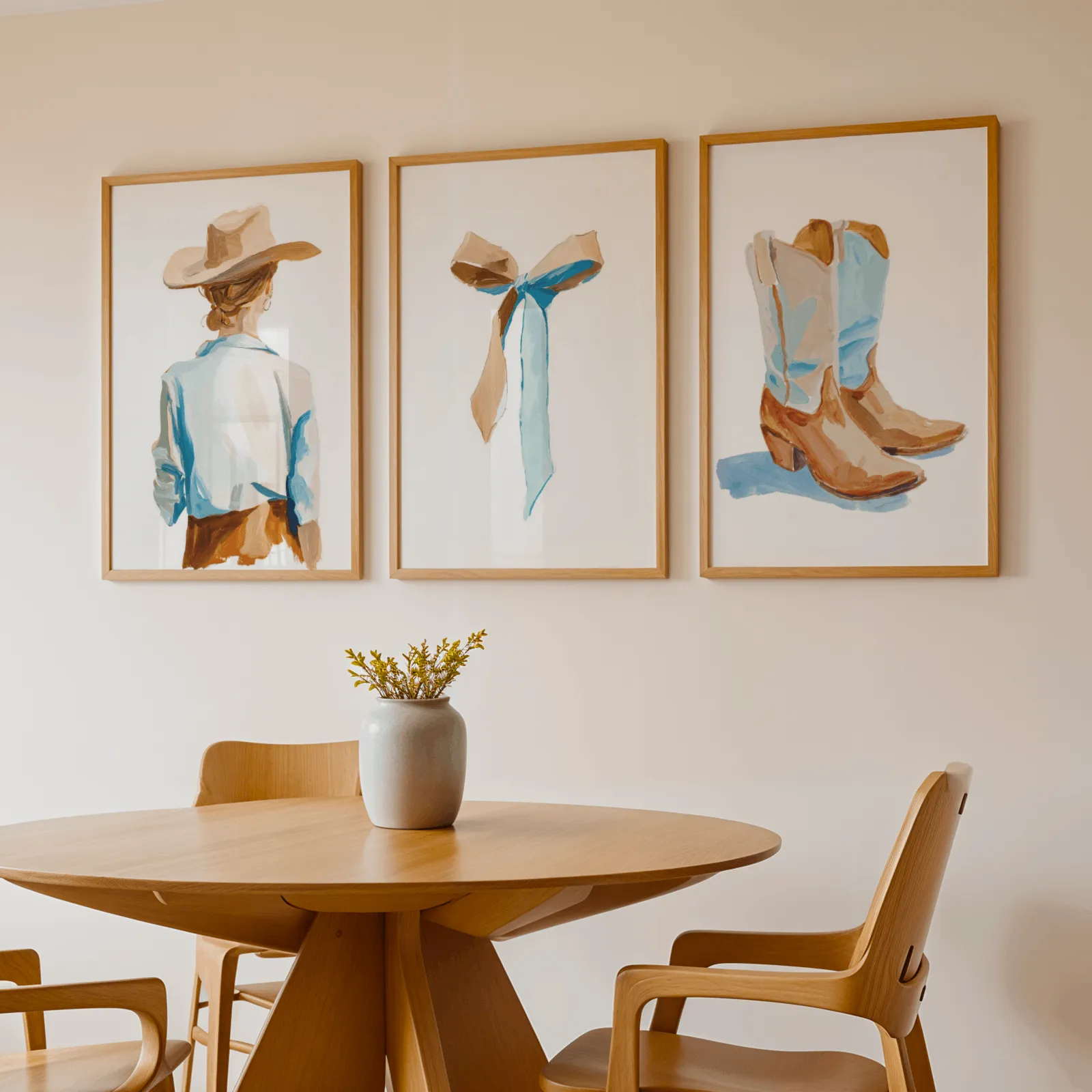 western cowgirl wall art set of 3 with hat ribbon and boots, above a round wooden table with a stoneware vase