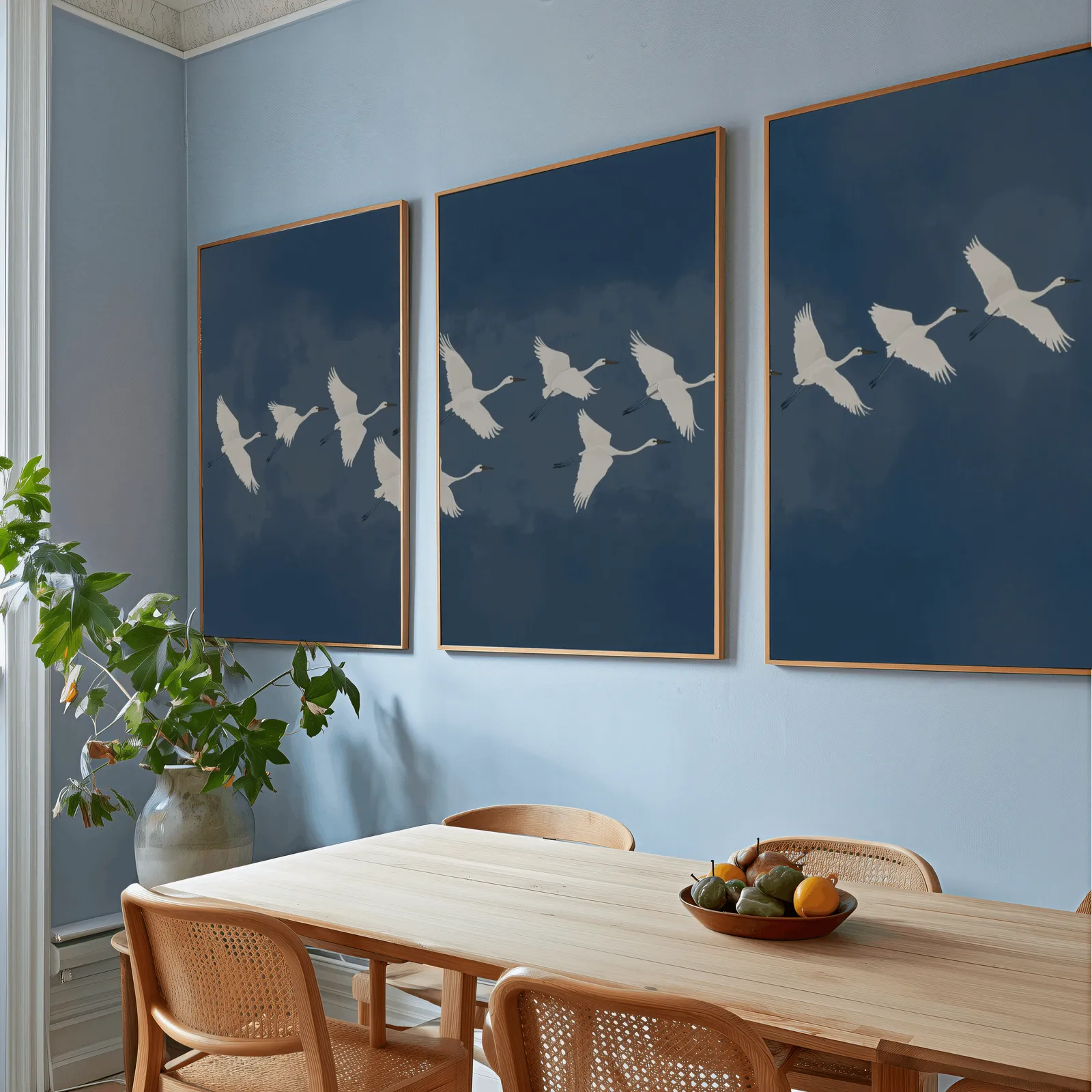 blue crane triptych wall art set, above a wooden dining table with cane chairs and a fruit bowl