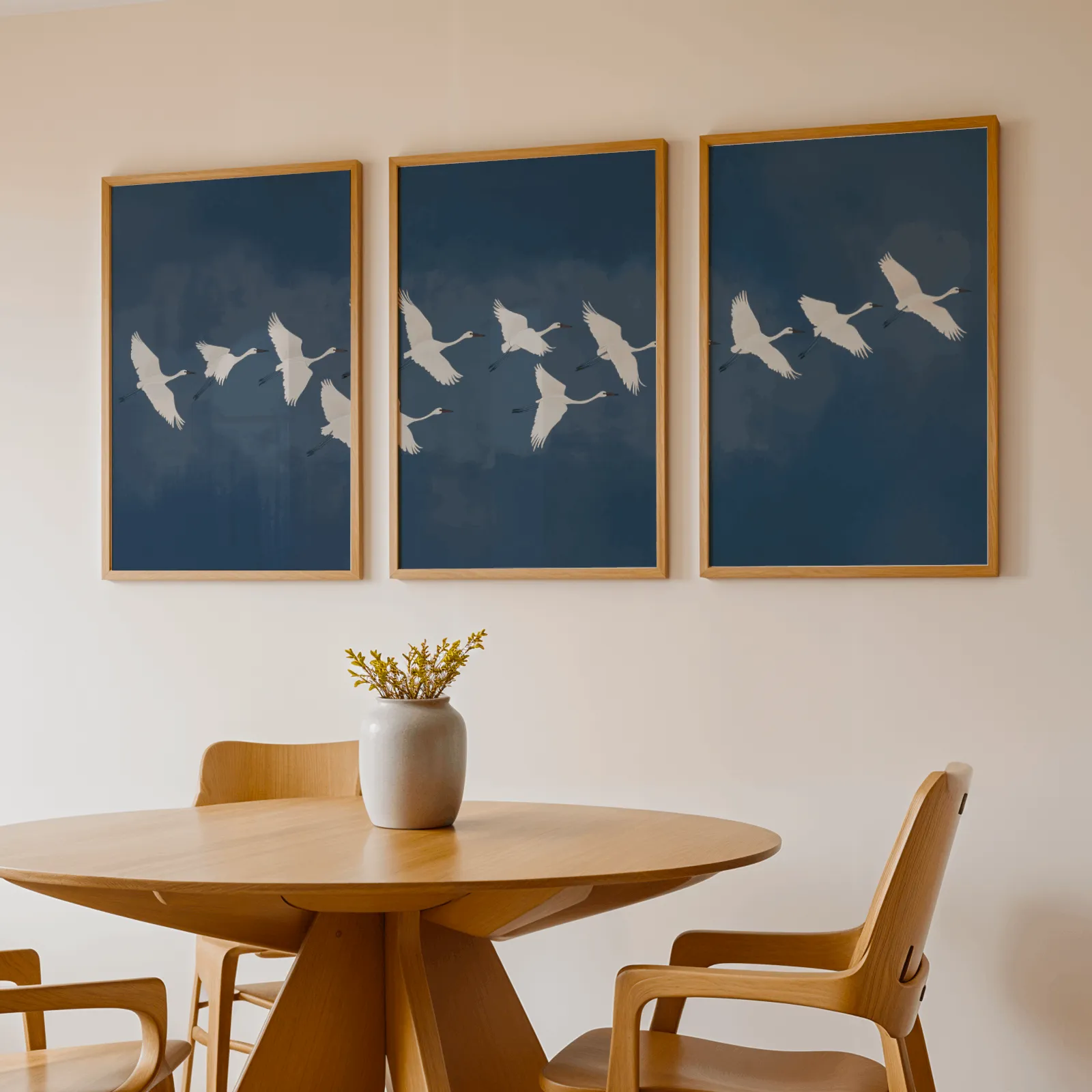 blue crane triptych wall art set, above a round wooden table with a stoneware vase