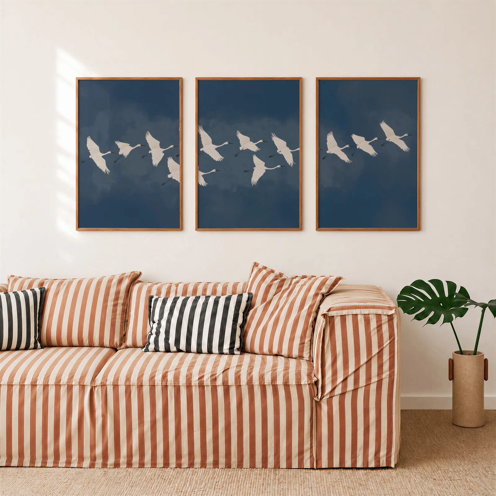 blue crane triptych wall art set, above a rust-striped sofa beside a potted monstera