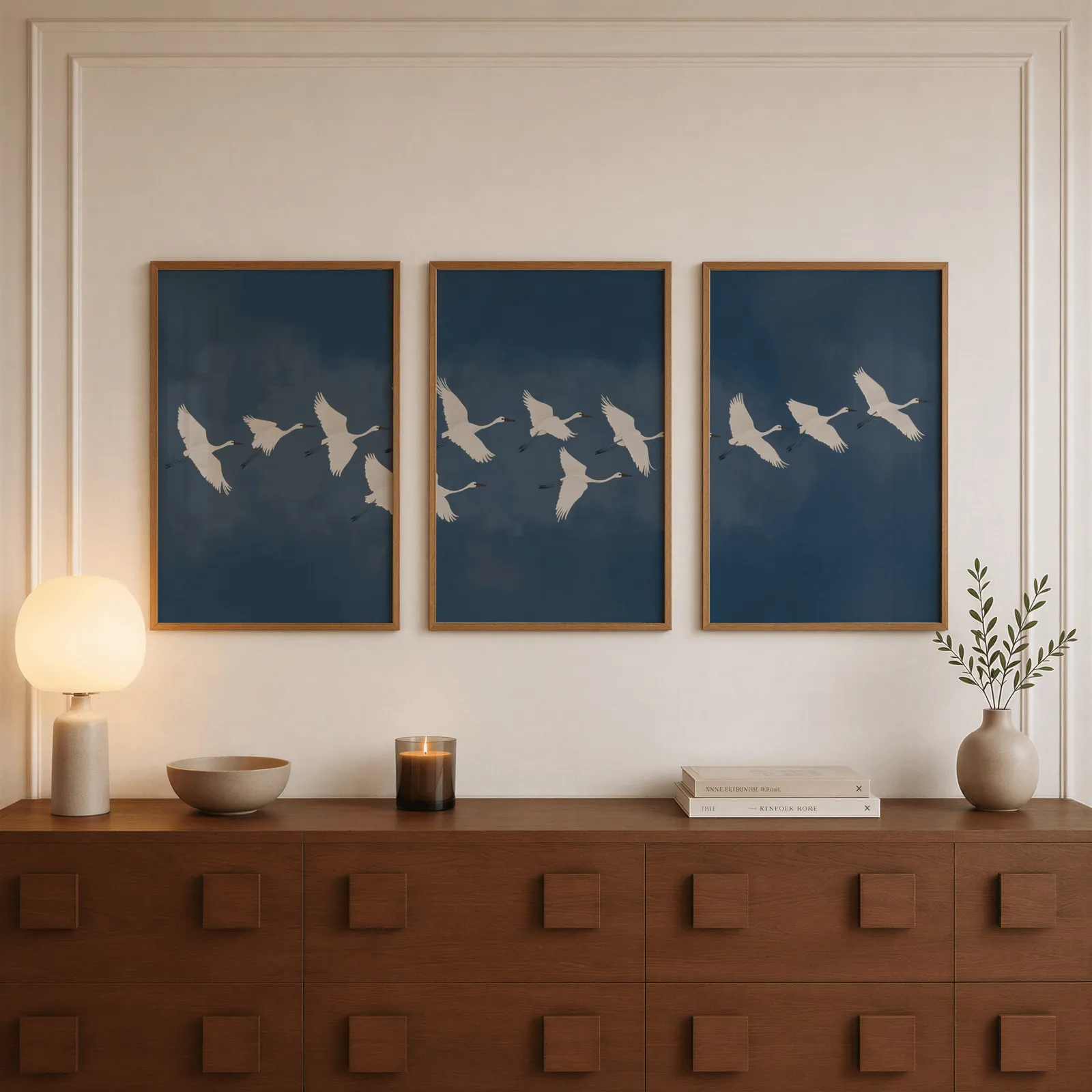 blue crane triptych wall art set, above a walnut sideboard with a lit candle and glowing lamp