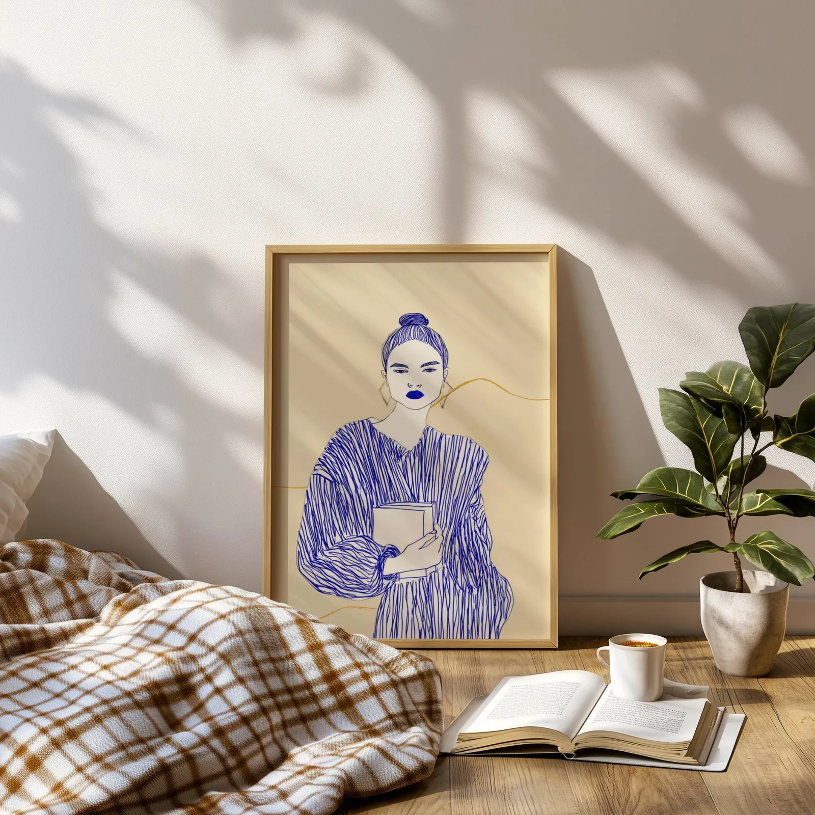 blue line art woman reading wall art, leaning on a sunlit floor beside a plaid blanket and open book