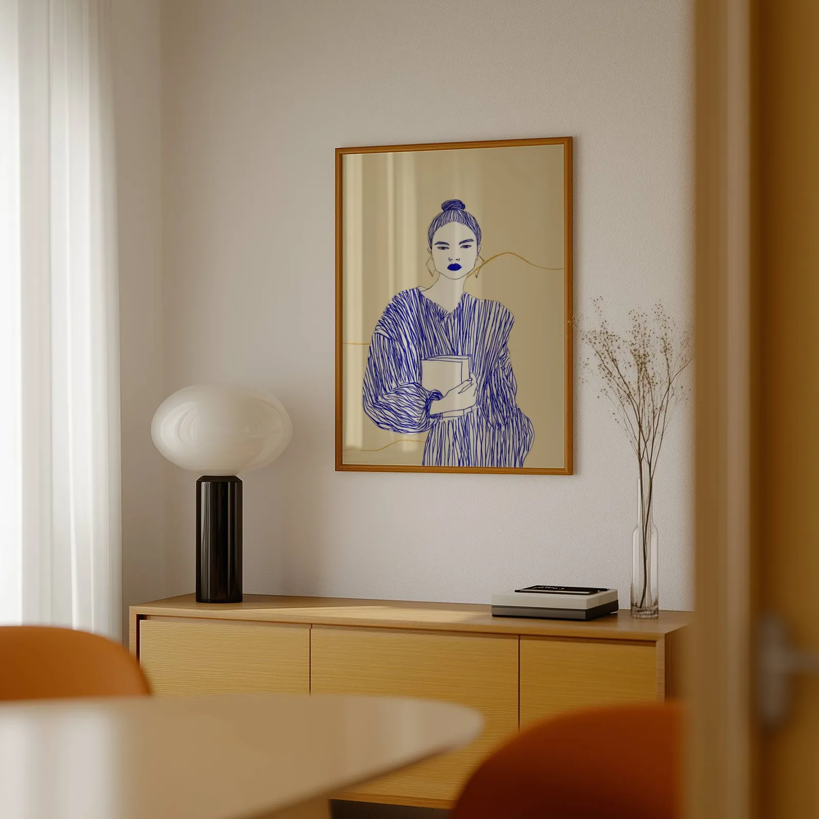 blue line art woman reading wall art, above a light wood sideboard beside a bulbous black lamp