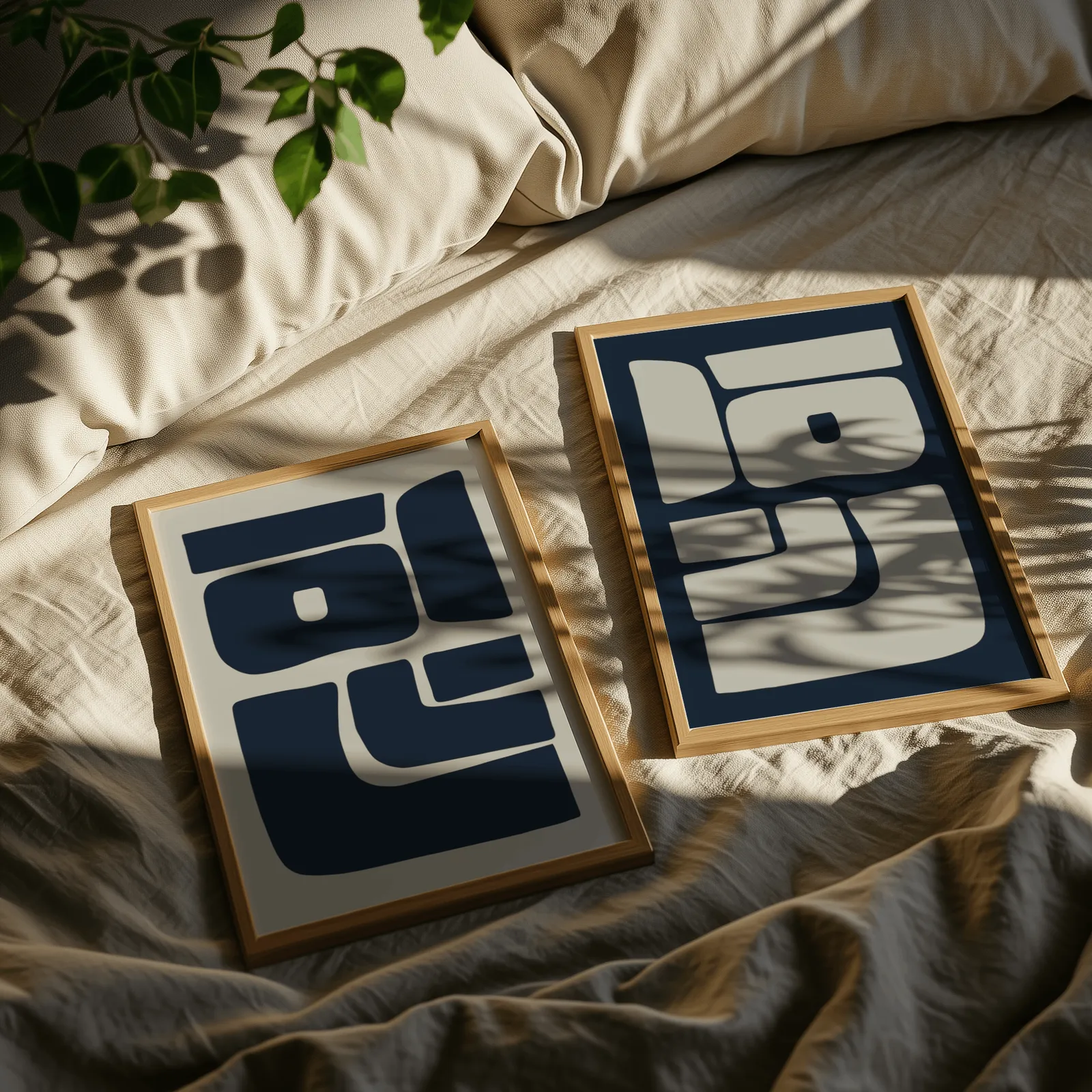 blue and grey abstract minimalist wall art set of two, resting on rumpled linen sheets with dappled leaf shadows