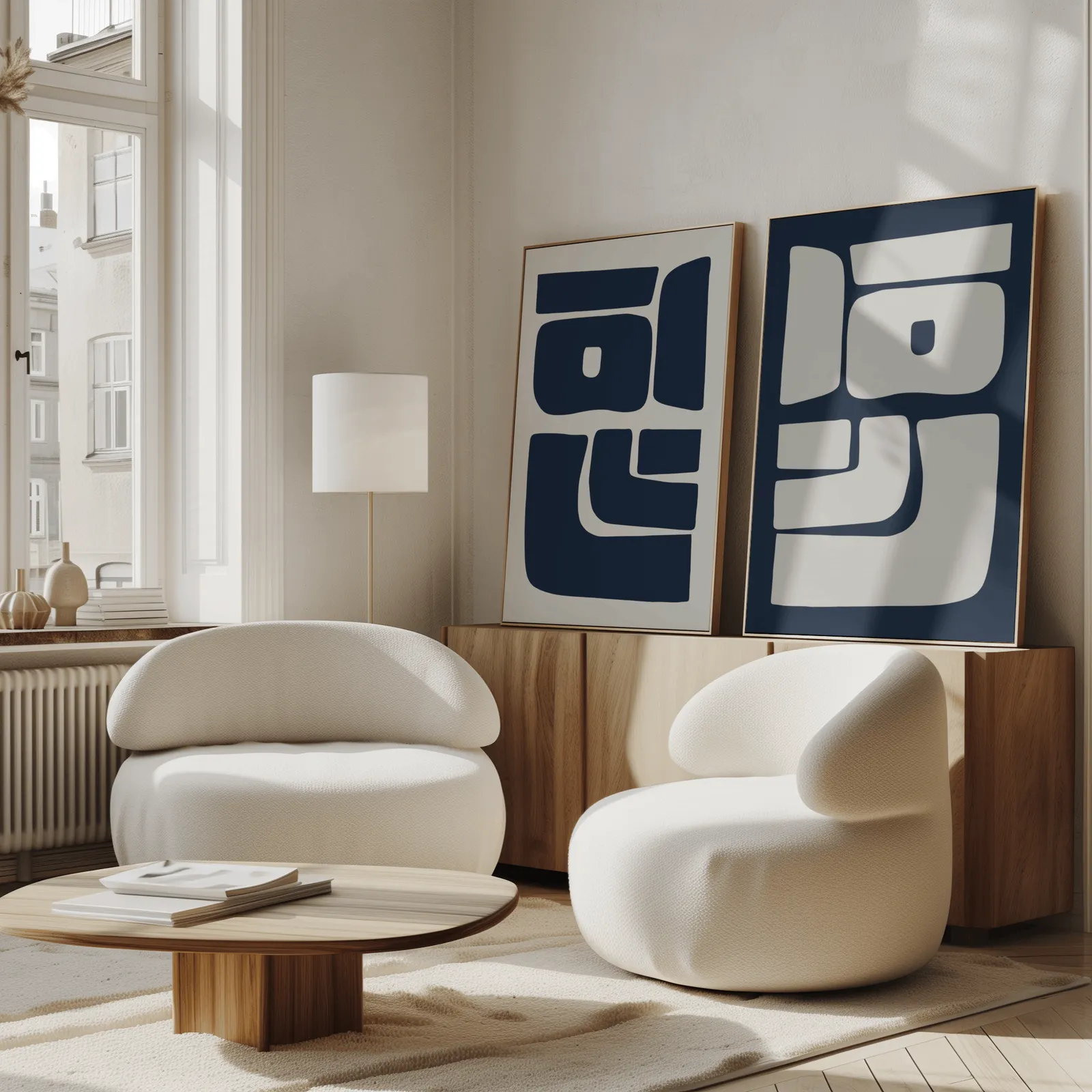 blue and grey abstract minimalist wall art set of two, propped against a wooden sideboard beside boucle armchairs