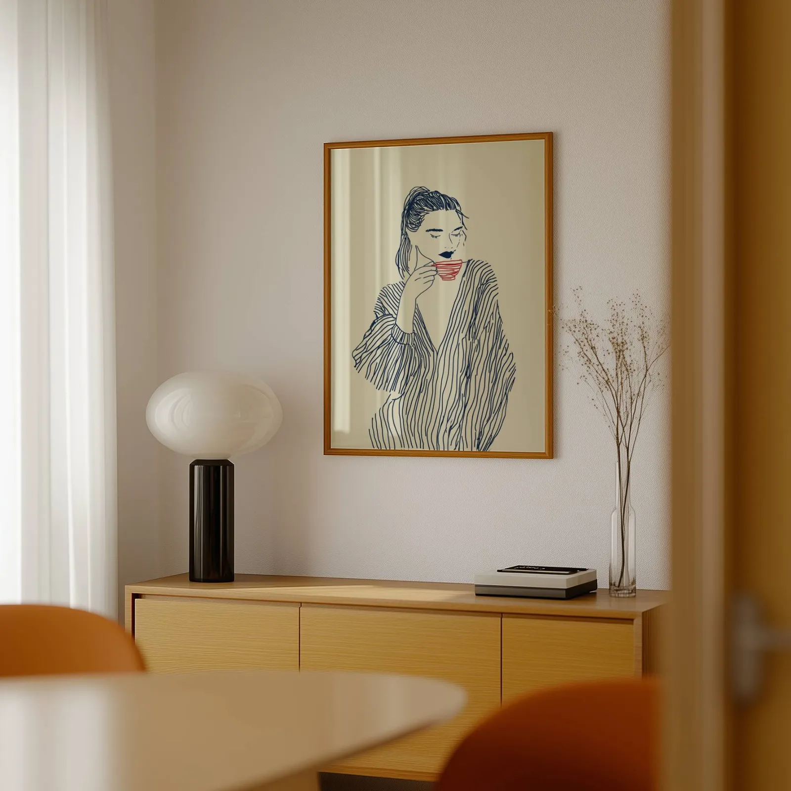 minimalist line art woman drinking coffee wall art, above a light wood sideboard beside a bulbous black lamp
