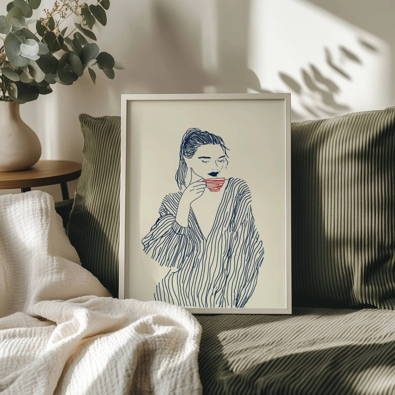 minimalist line art woman drinking coffee wall art, propped on an olive corduroy sofa beside a eucalyptus vase