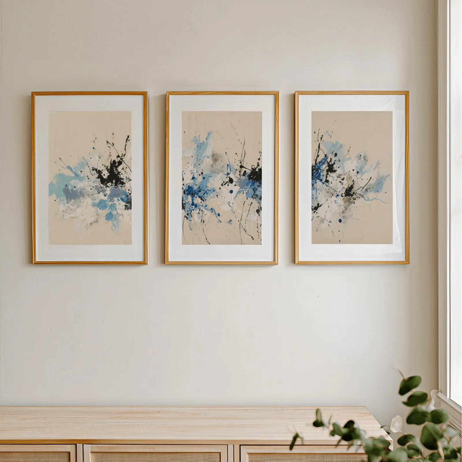 blue and black abstract splatter triptych wall art, in a row above a light wooden sideboard near a window
