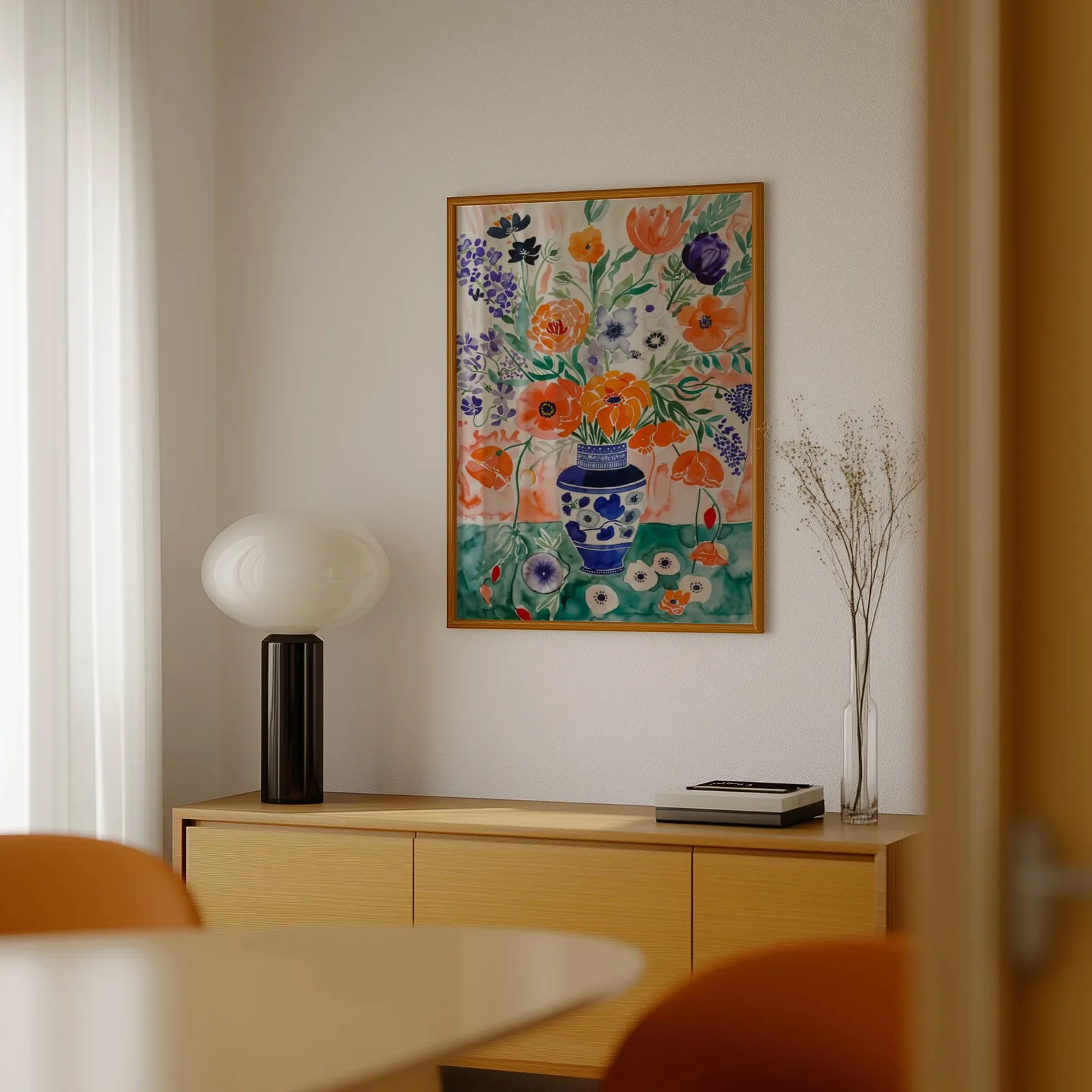 colorful floral wall art with blue vase, above a light wood sideboard beside a bulbous black lamp