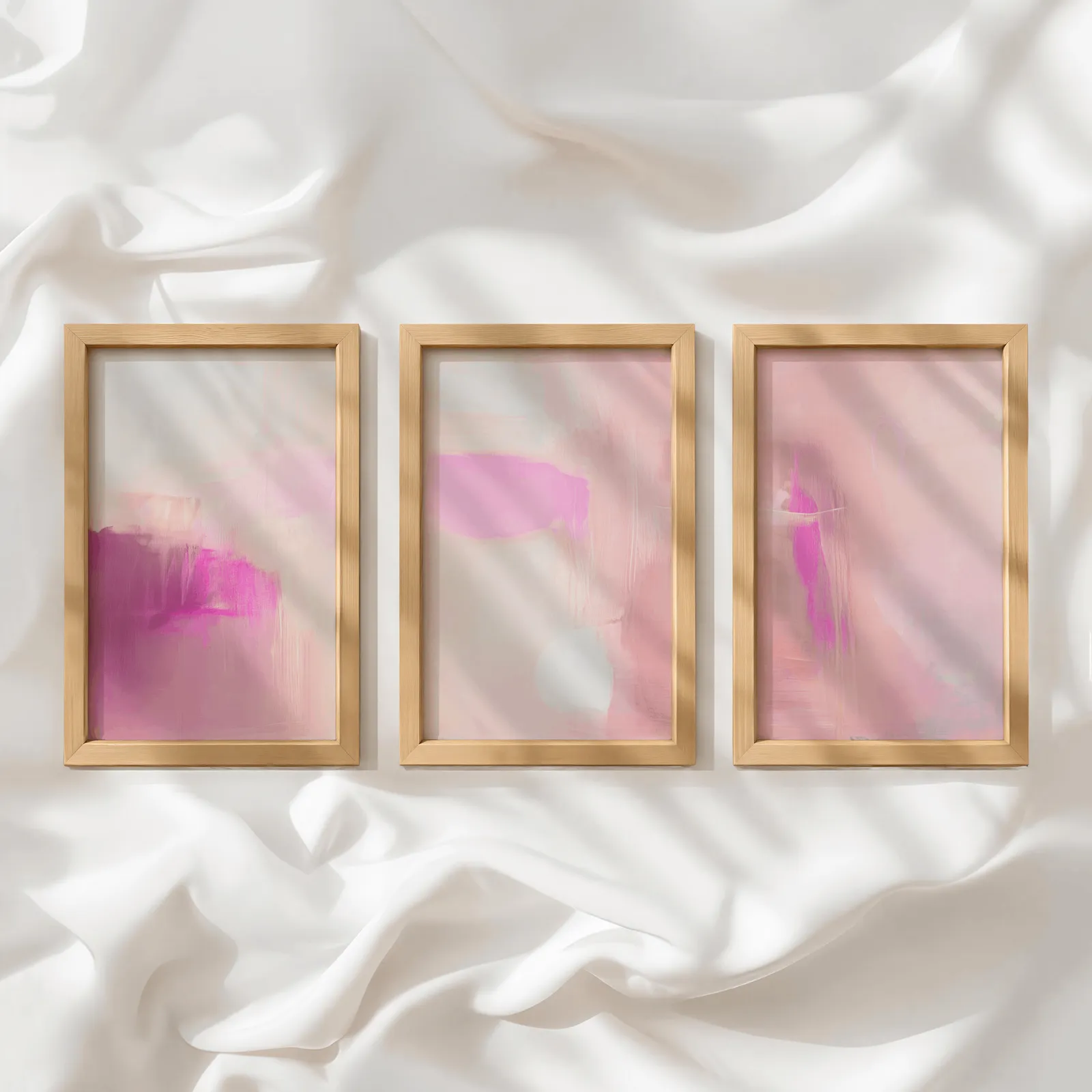 pink abstract set of 3 wall art, in a row atop rumpled white silky fabric