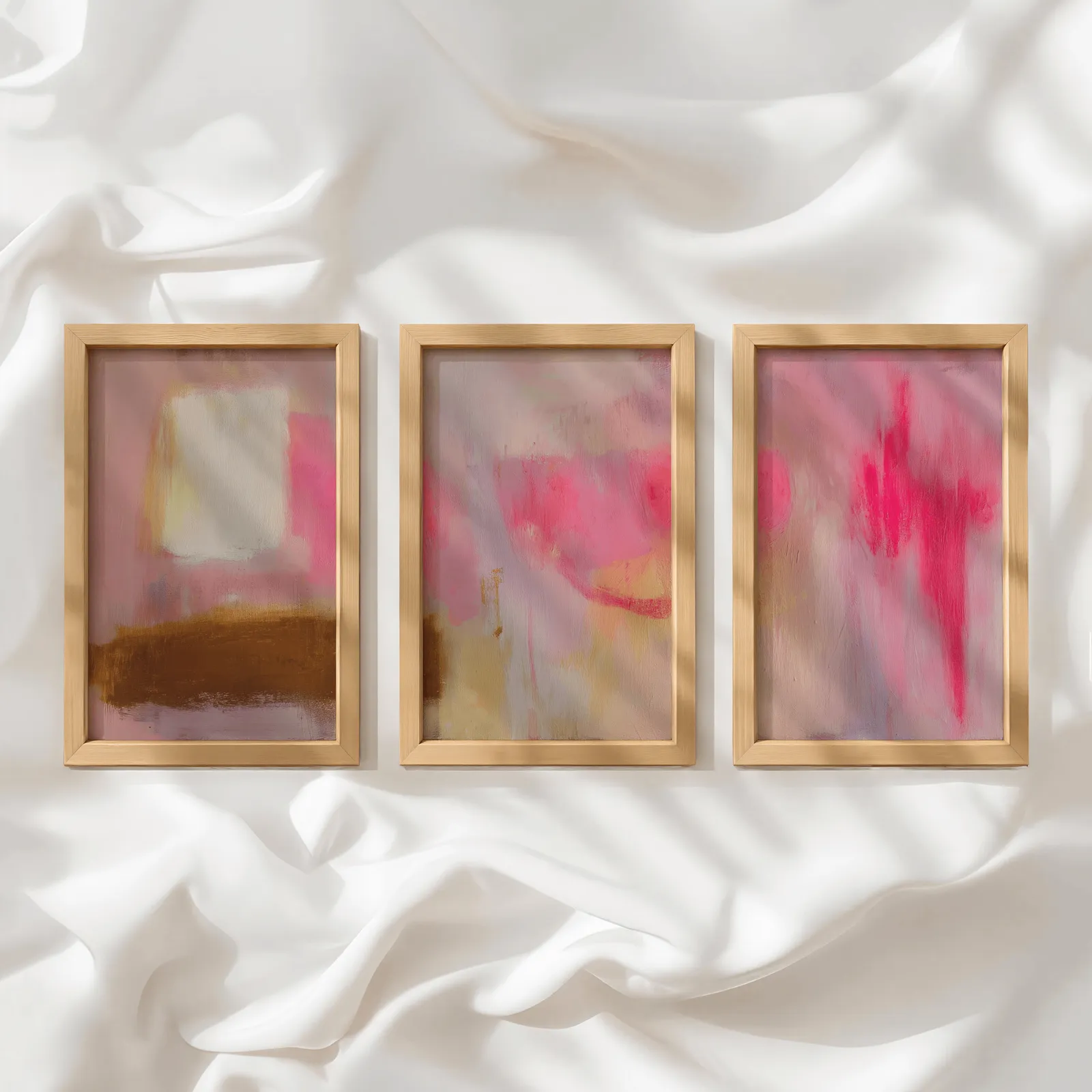 pink abstract wall art set of 3, in a row atop rumpled white silky fabric
