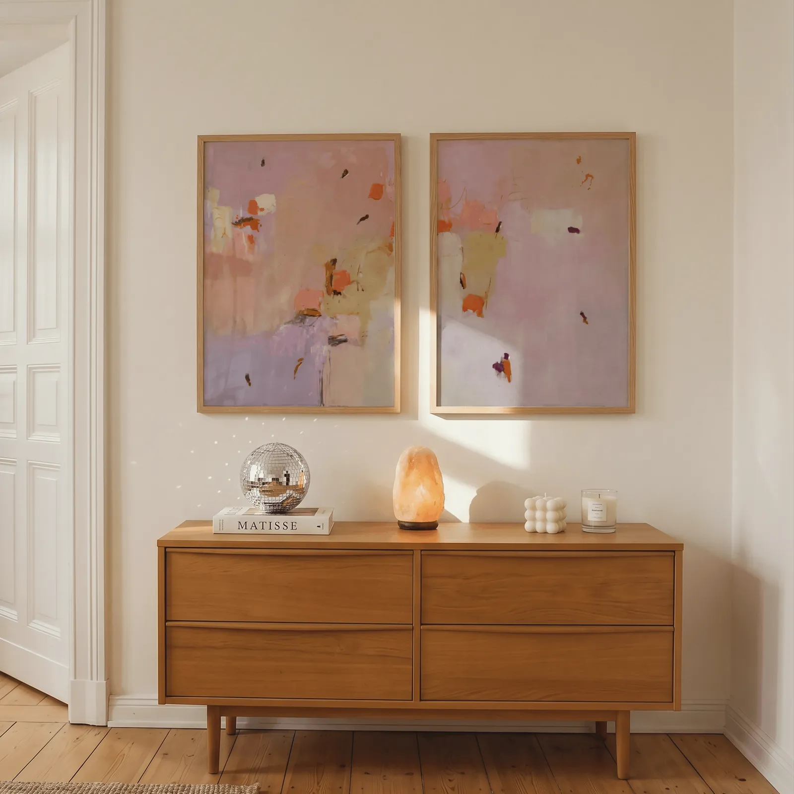 pink abstract wall art set of two, above a wooden dresser with a salt lamp and disco ball
