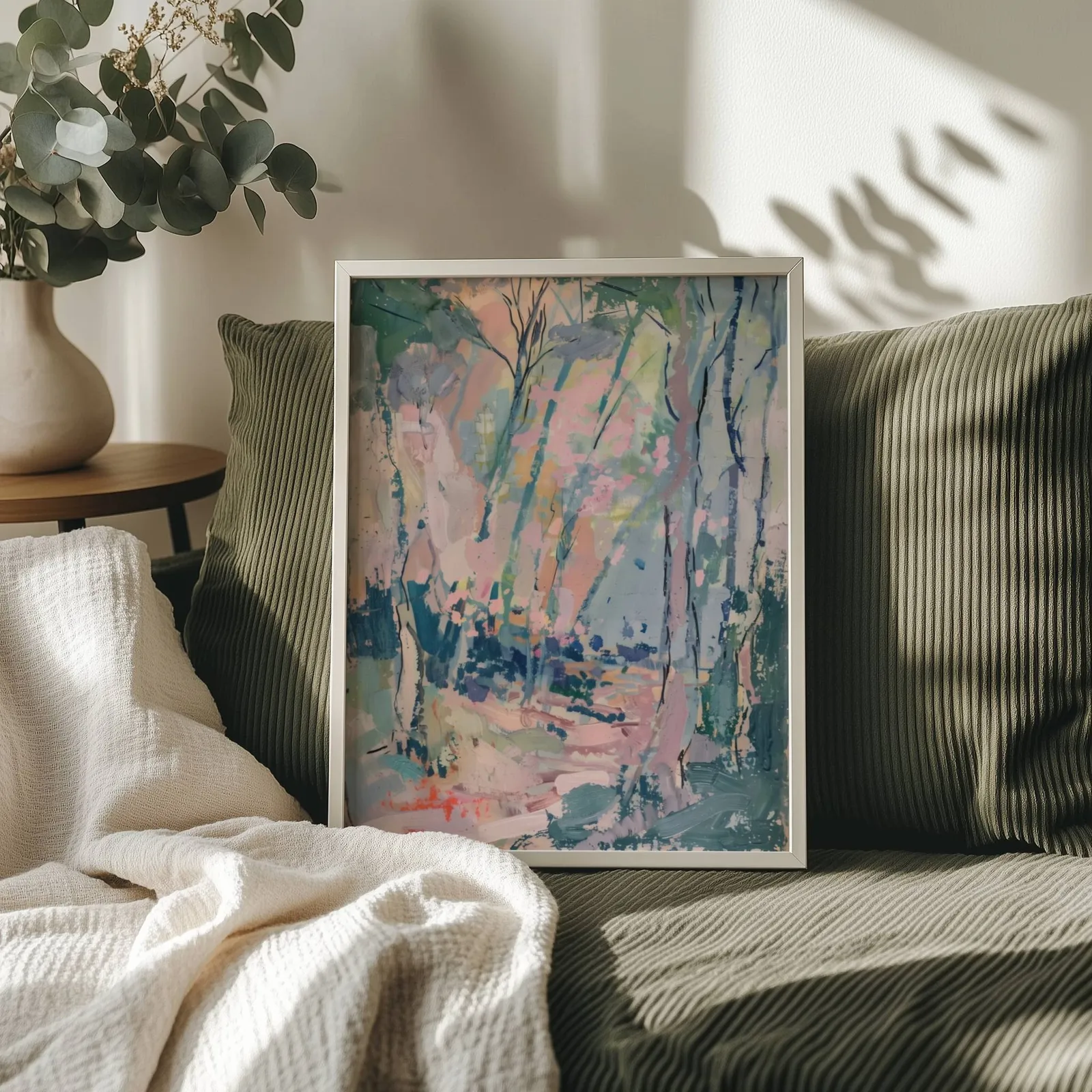 pink and green abstract forest wall art, propped on an olive corduroy sofa beside a eucalyptus vase