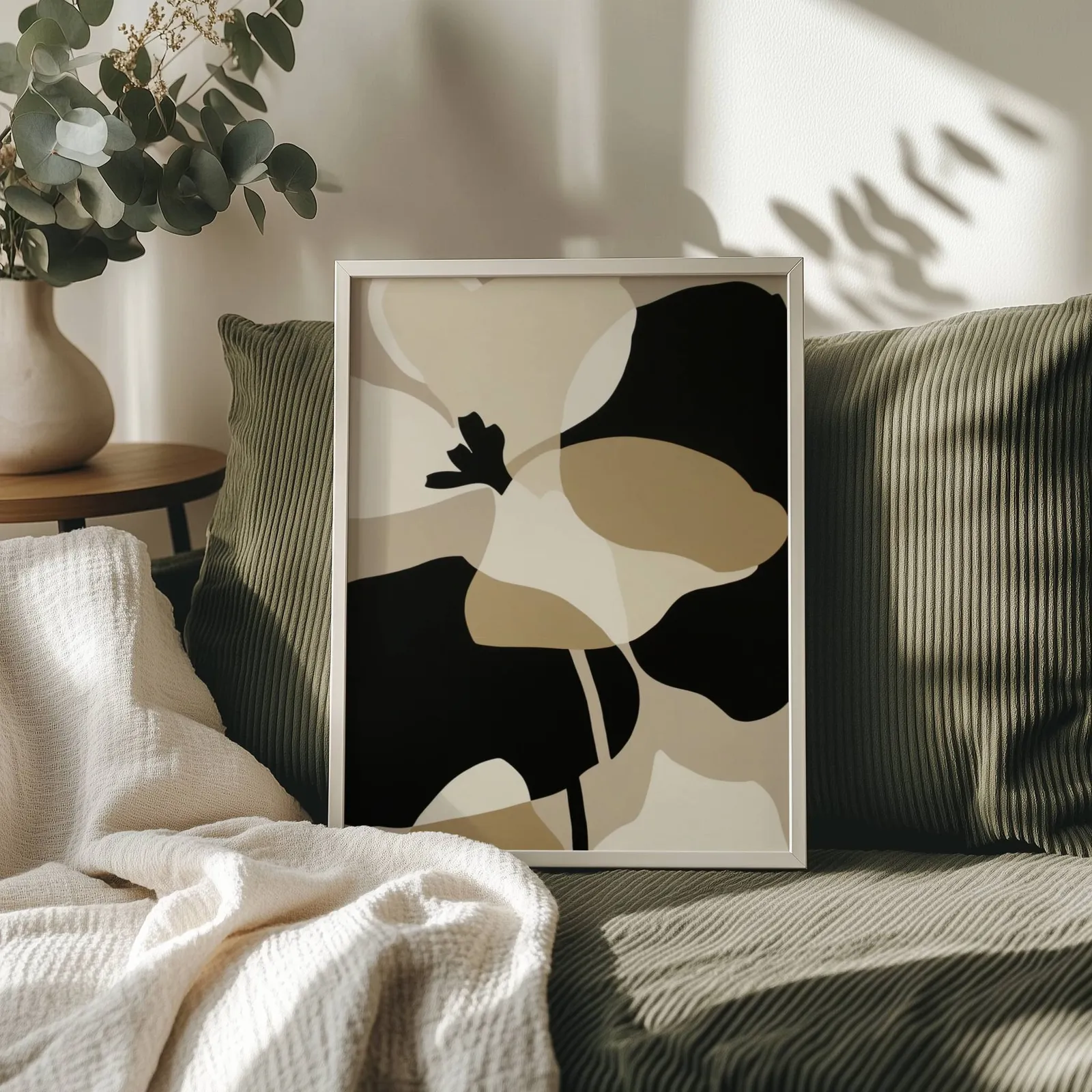 black and beige abstract botanical wall art, propped on an olive corduroy sofa beside a eucalyptus vase