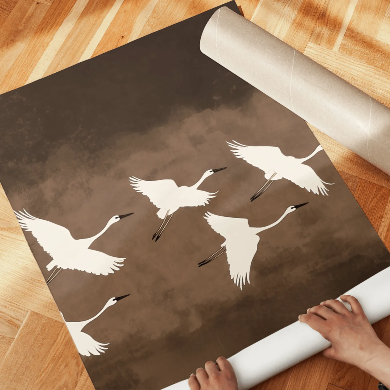 brown minimalist crane wall art set of three, unrolled across a herringbone wood floor by hand