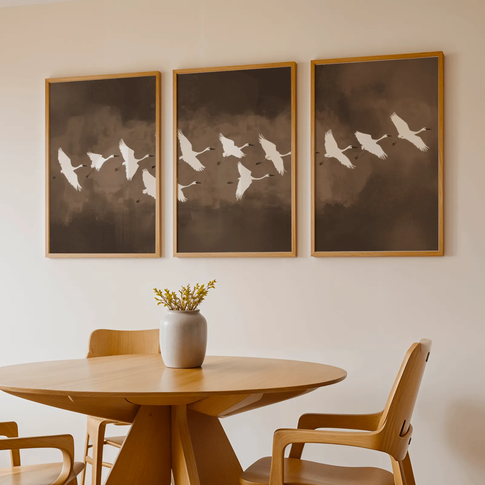 brown minimalist crane wall art set of three, above a round wooden table with a stoneware vase