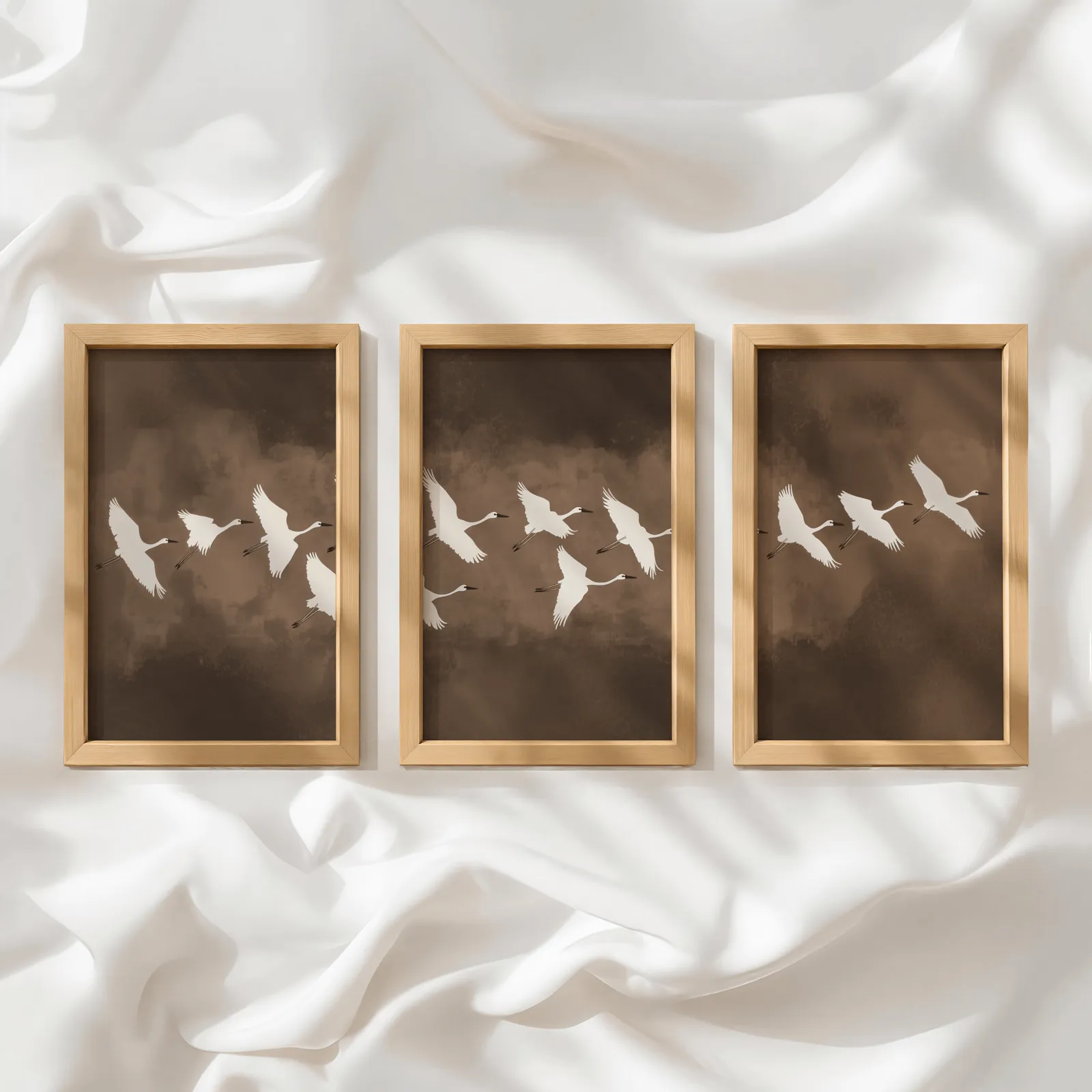 brown minimalist crane wall art set of three, in a row atop rumpled white silky fabric