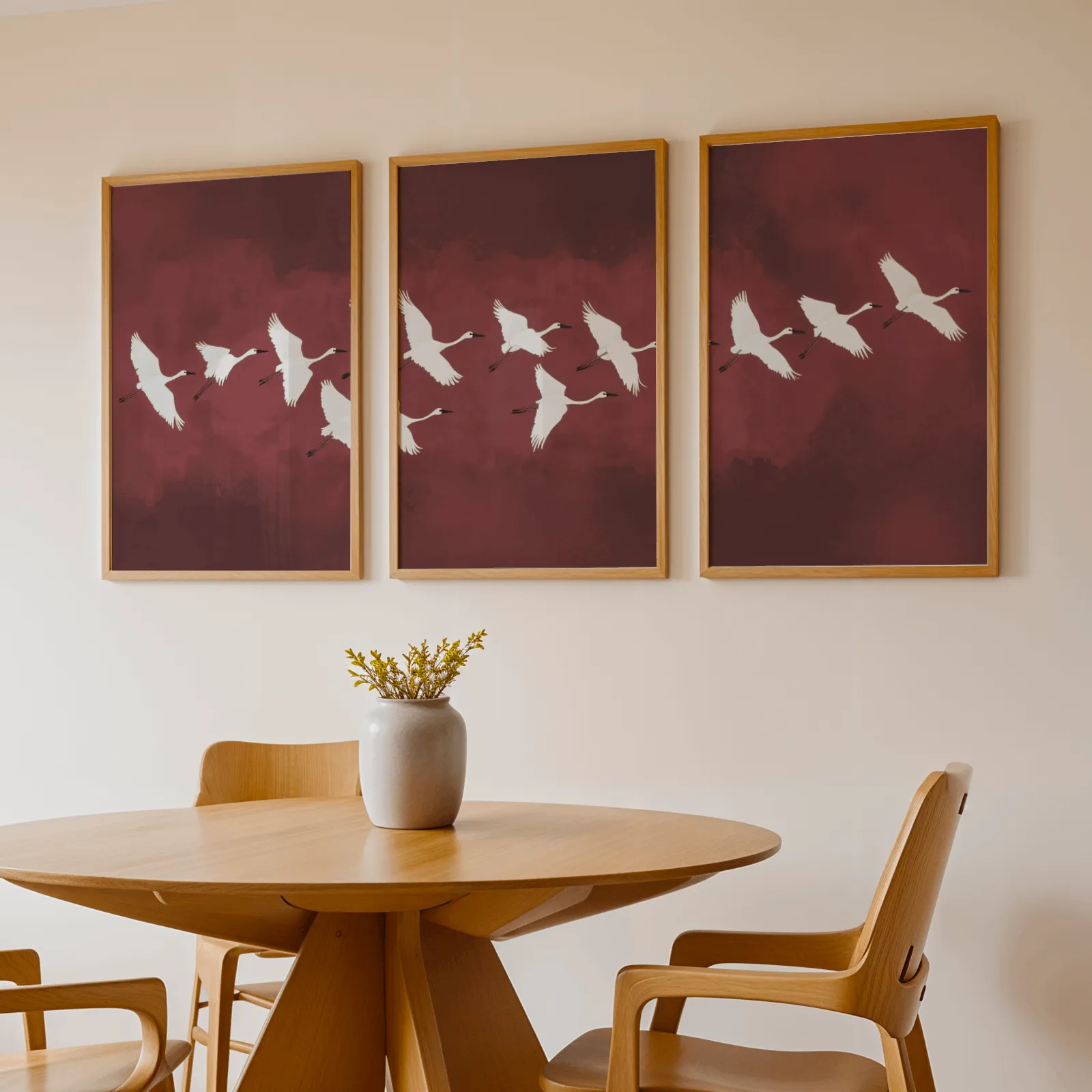 burgundy crane flight triptych wall art, above a round wooden table with a stoneware vase