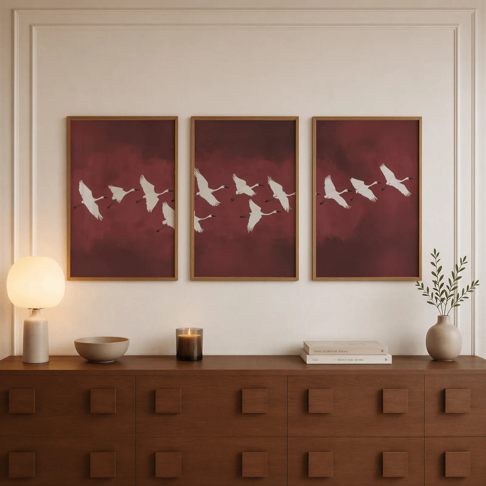 burgundy crane flight triptych wall art, above a walnut sideboard with a lit candle and glowing lamp
