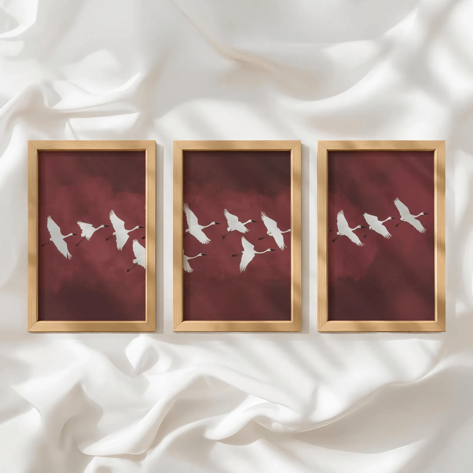 burgundy crane flight triptych wall art, in a row atop rumpled white silky fabric