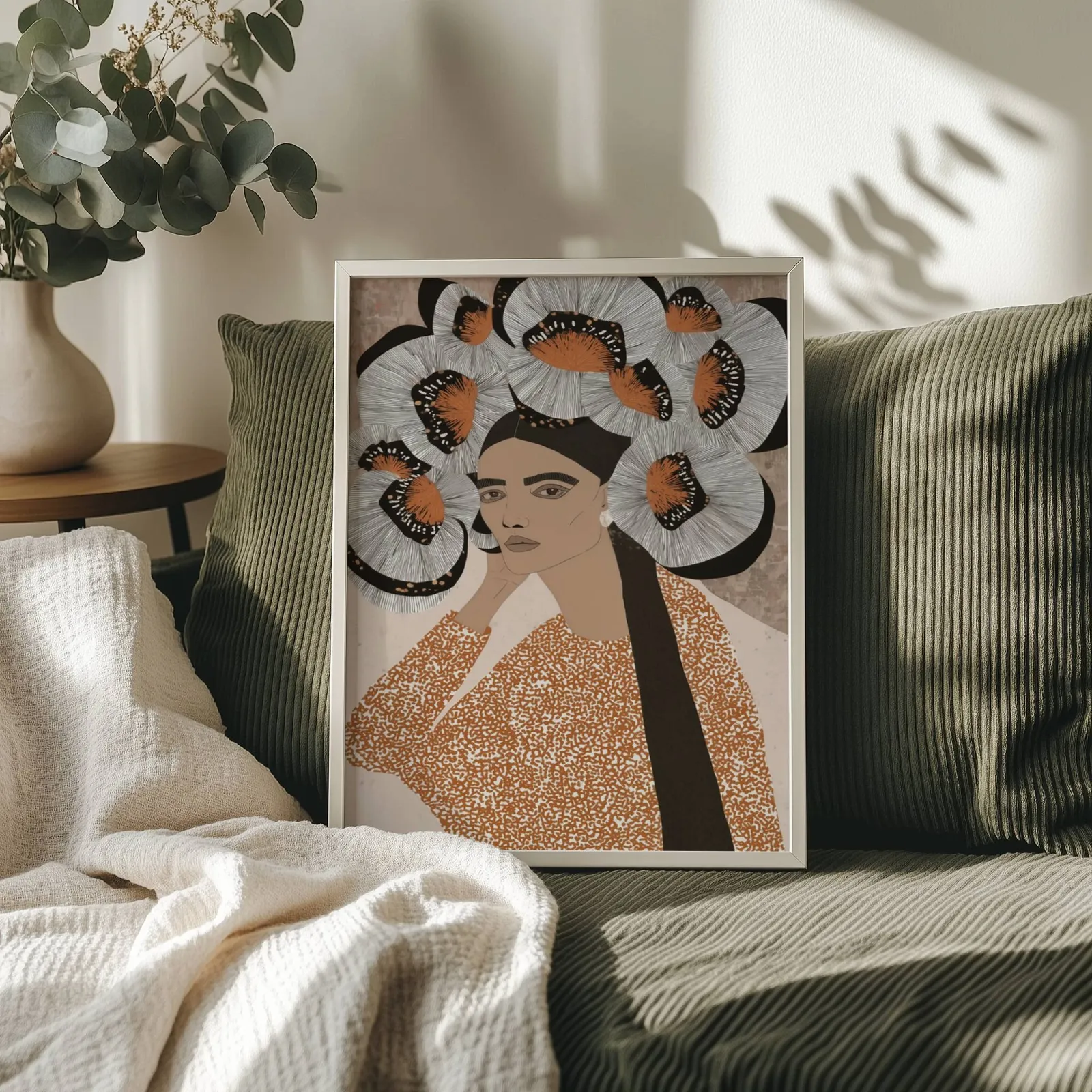 terracotta portrait wall art with butterfly crown, propped on an olive corduroy sofa beside a eucalyptus vase
