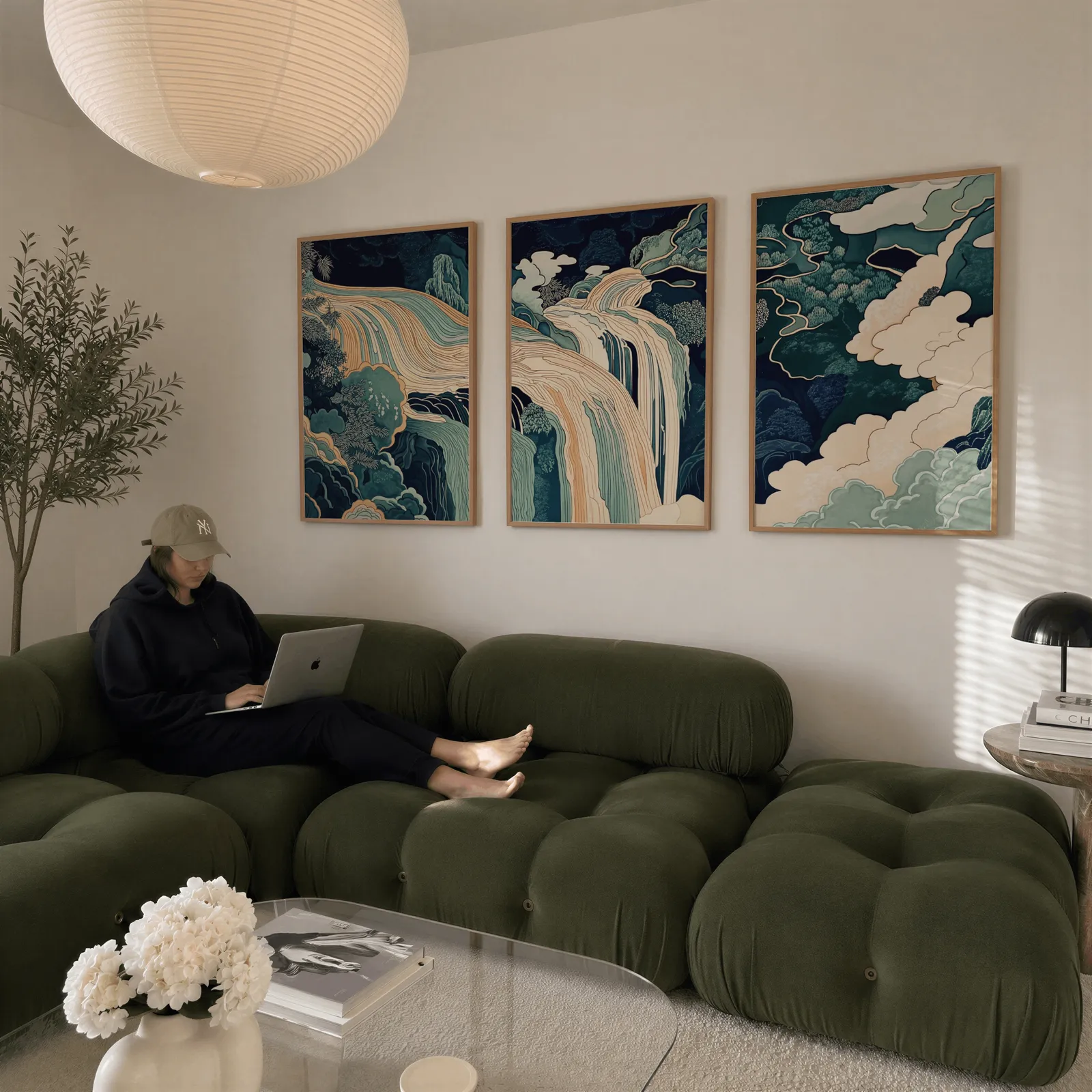 blue green waterfall landscape triptych wall art, above a plush olive velvet sectional beneath a paper lantern light