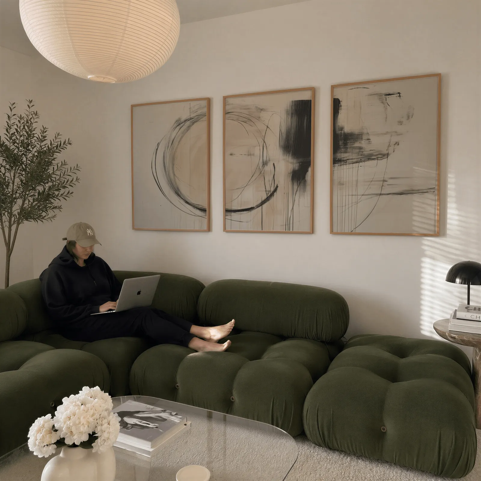 beige abstract minimalist wall art set of three, above a plush olive velvet sectional beneath a paper lantern light